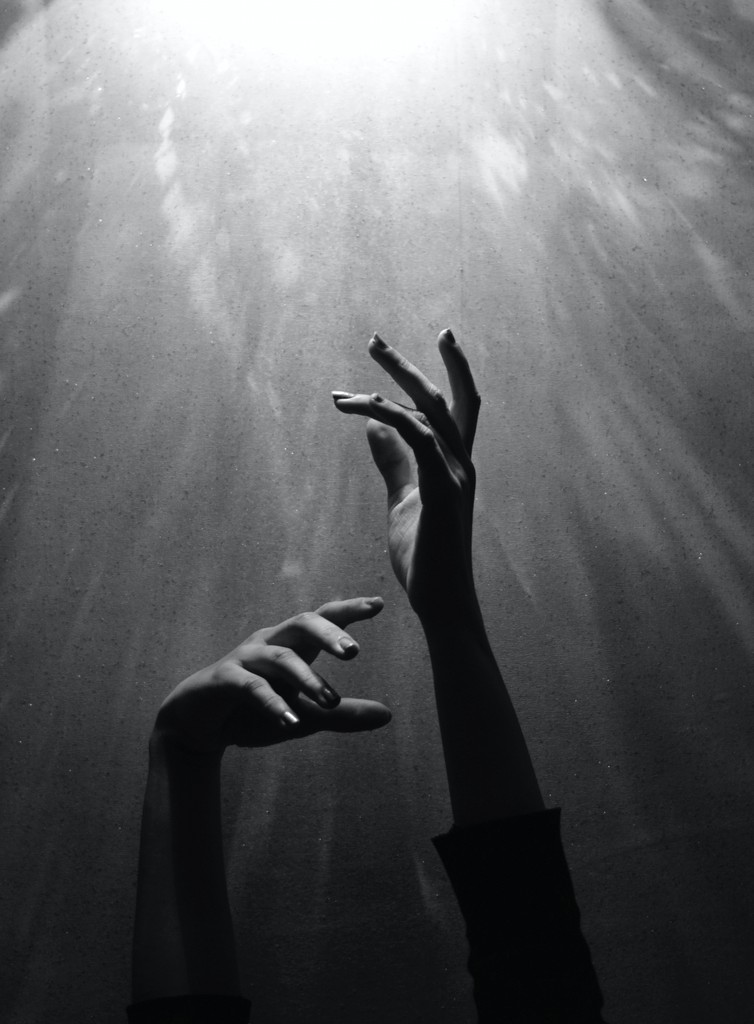 black white image showing hands under water reaching up to the surface