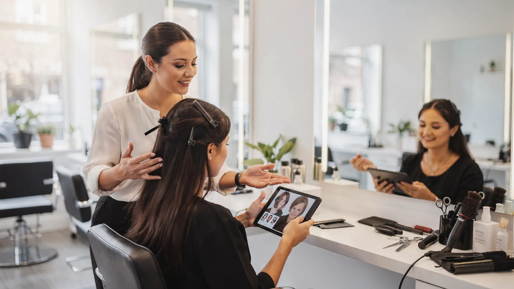 A salon consultation scene with a stylist gently sectioning a client's hair while discussing face shape, hair length, texture, and haircut inspiration photos in a bright modern salon.