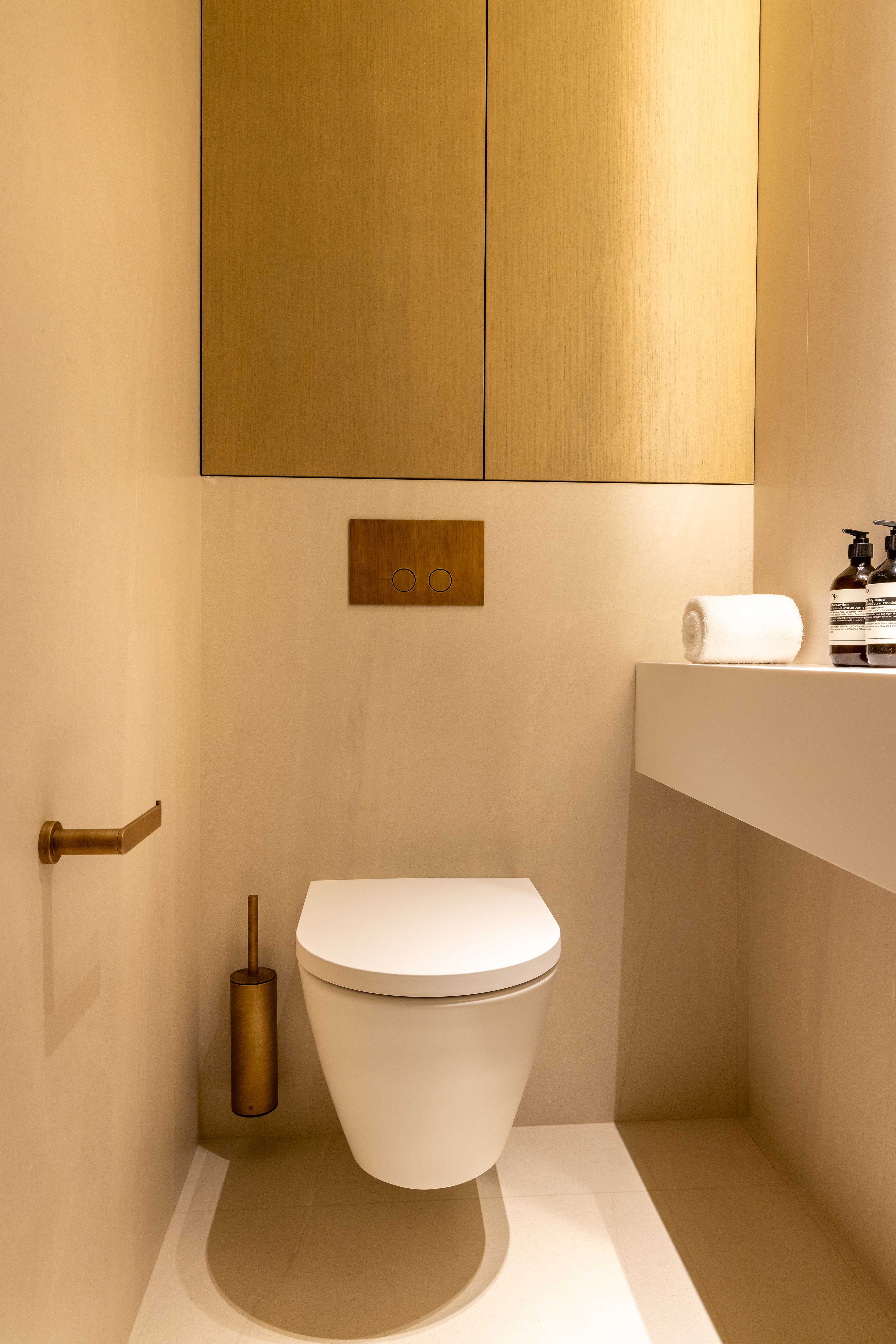 Toilettes suspendues blanches avec accessoires dorés, rangement en bois et étagère avec produits