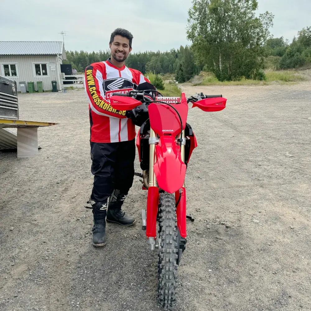 Sreehas in full motocross gear standing next to a red dirt bike