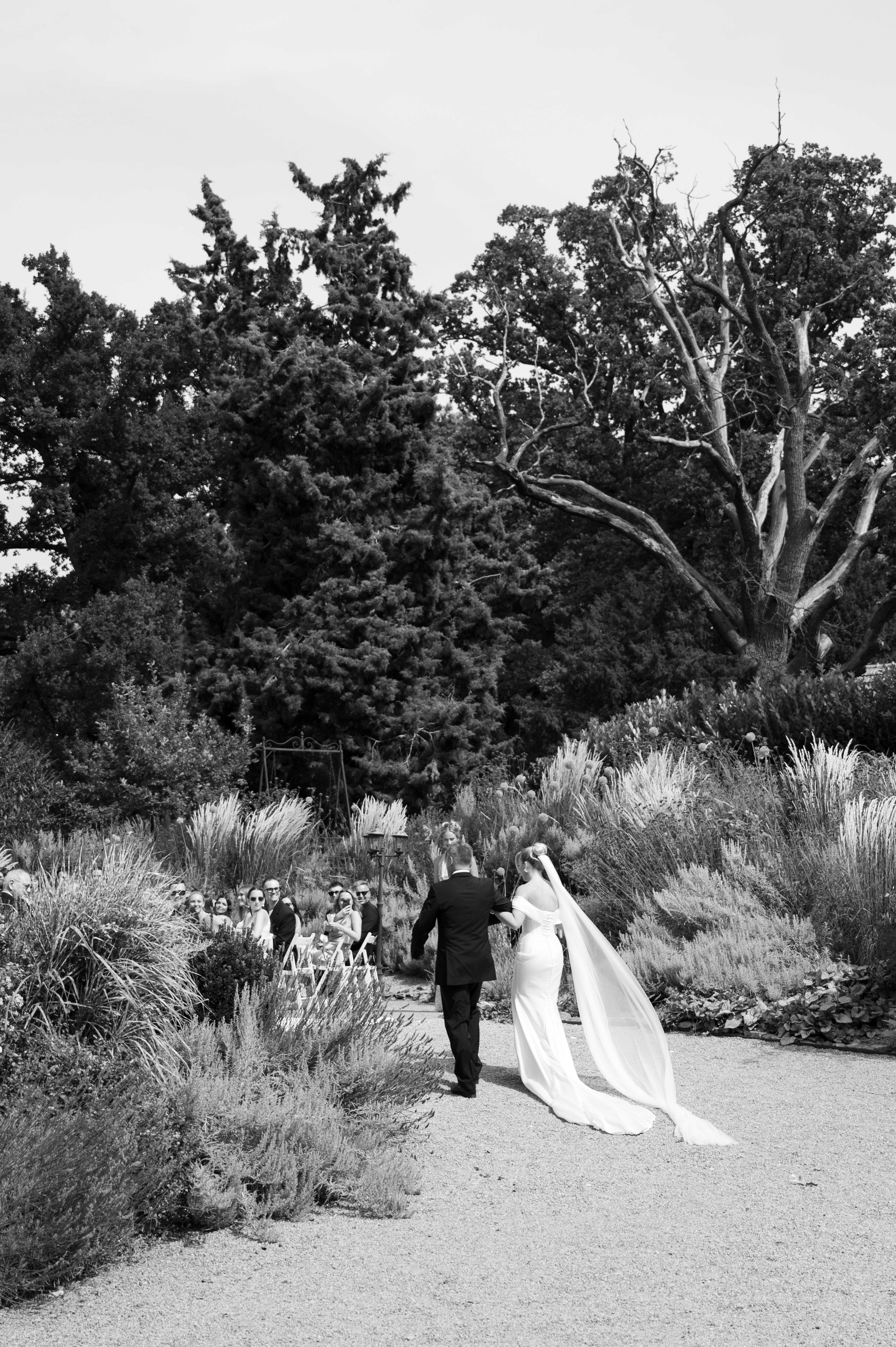 Bride and groom walking through tall garden grass in black and white — intimate, cinematic, timeless.