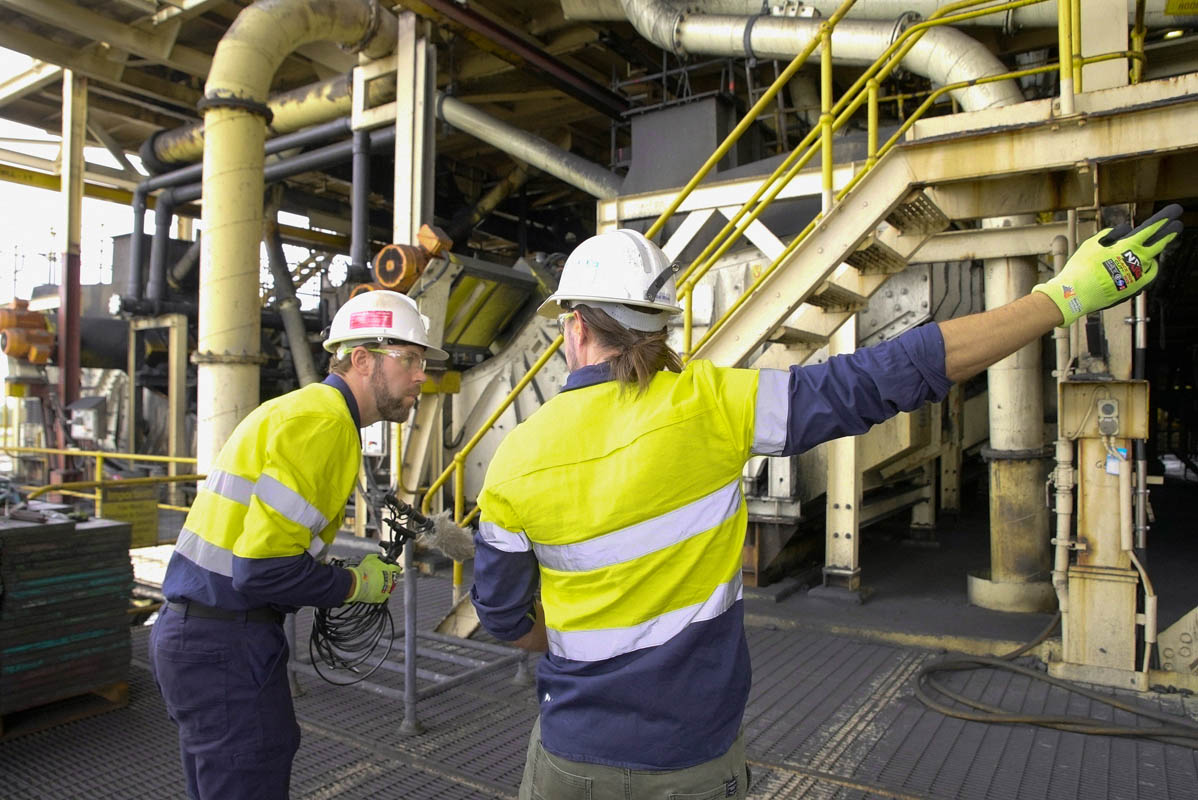Two workers in high-vis PPE on industrial site staircase pointing at equipment