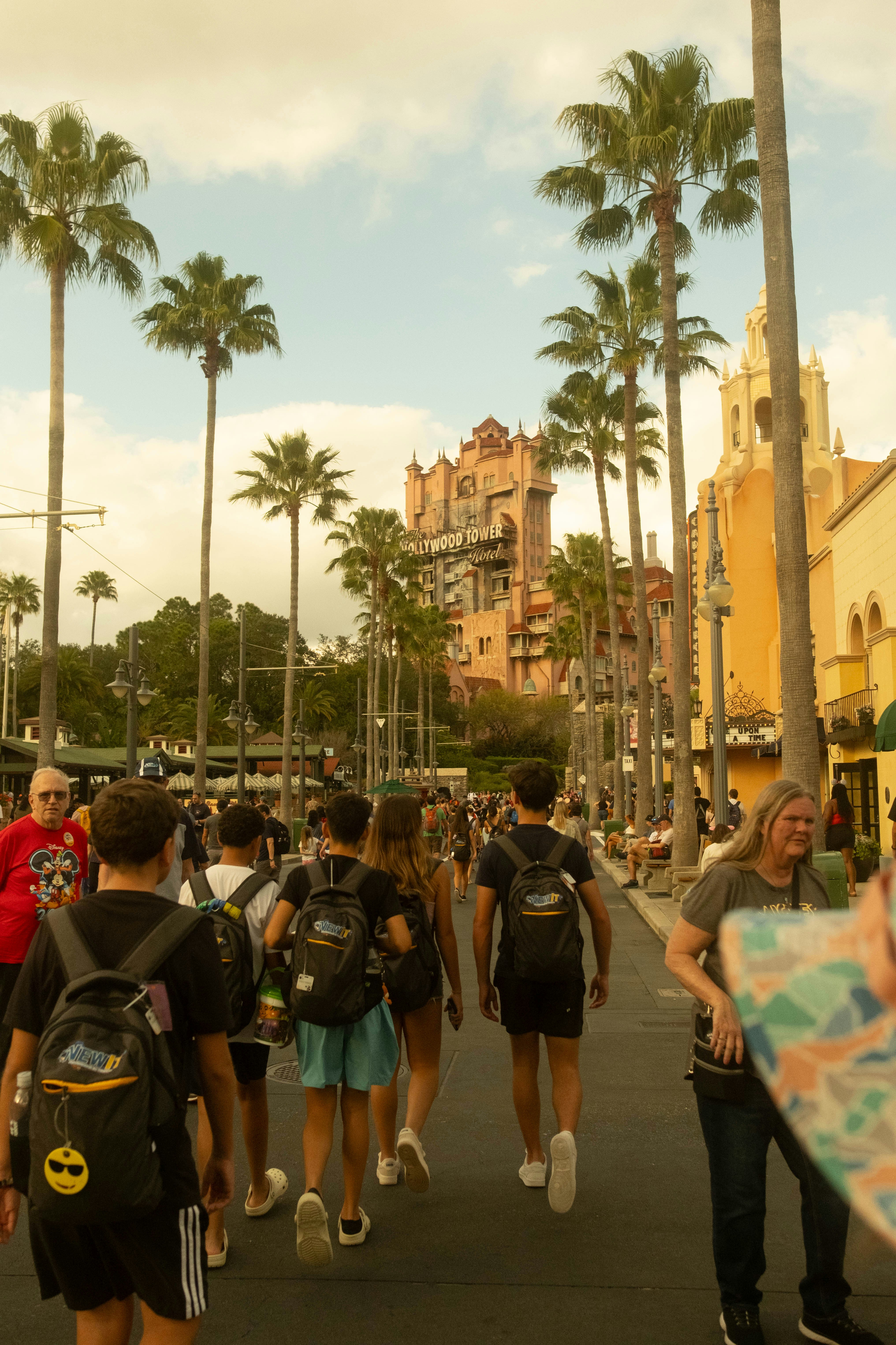 People walking down a street lined with palm trees.