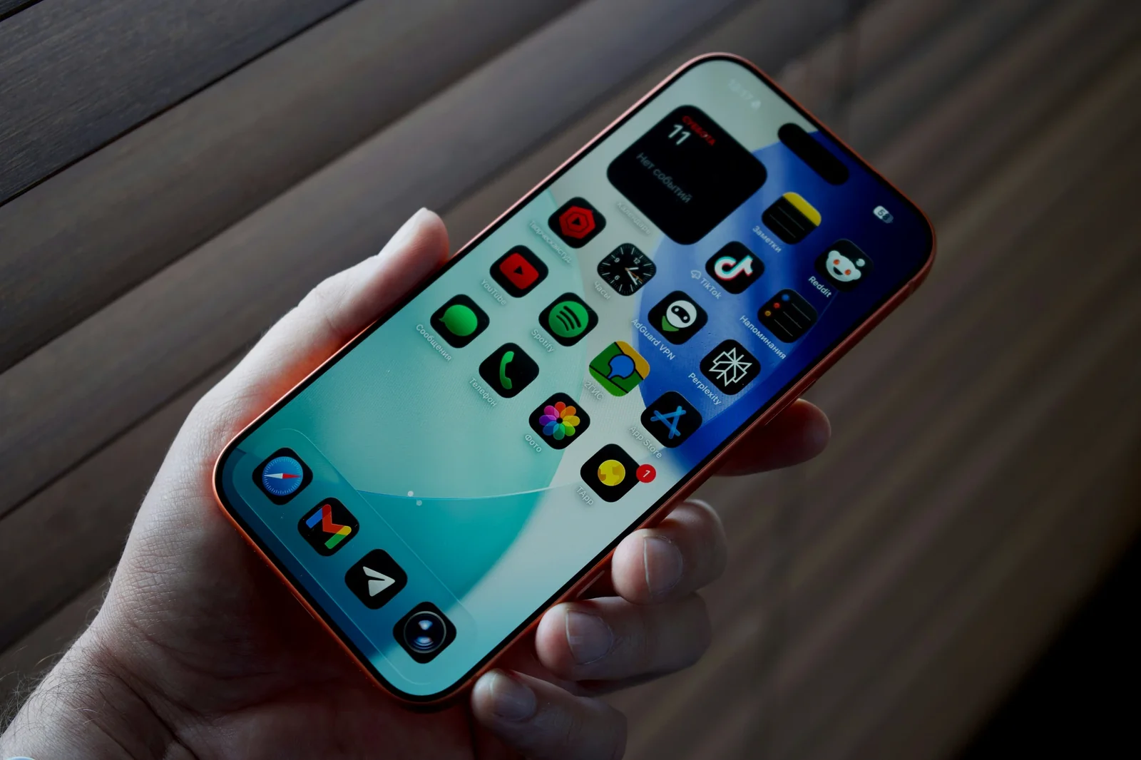 Person holding red iPhone displaying colorful app icons including Spotify, Photos, and App Store on home screen.
