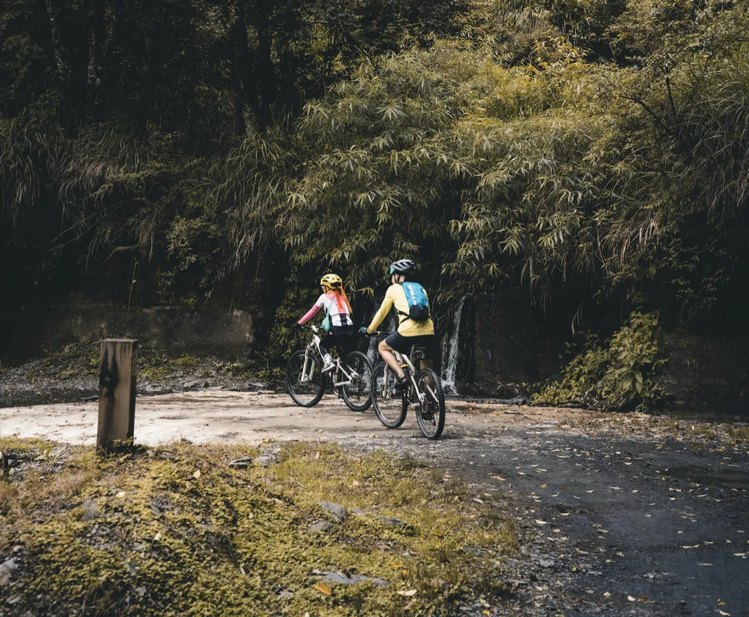 two adventurous cyclists with backpacks ride across a muddy road