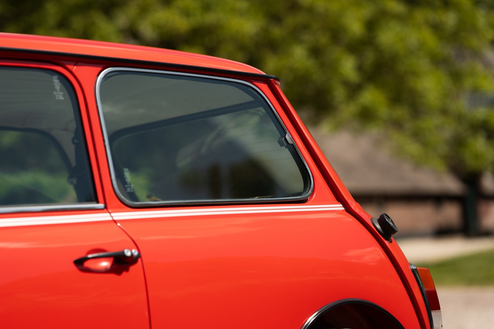 Close-up of the back corner of a bright red car parked outdoors, with greenery in the background.