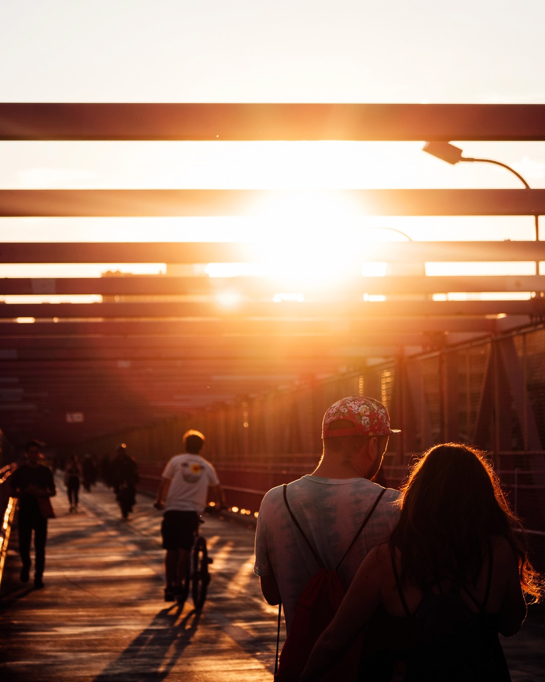 Orange toned sunset photo of two people walking across the williamsburg bridge in nyc.