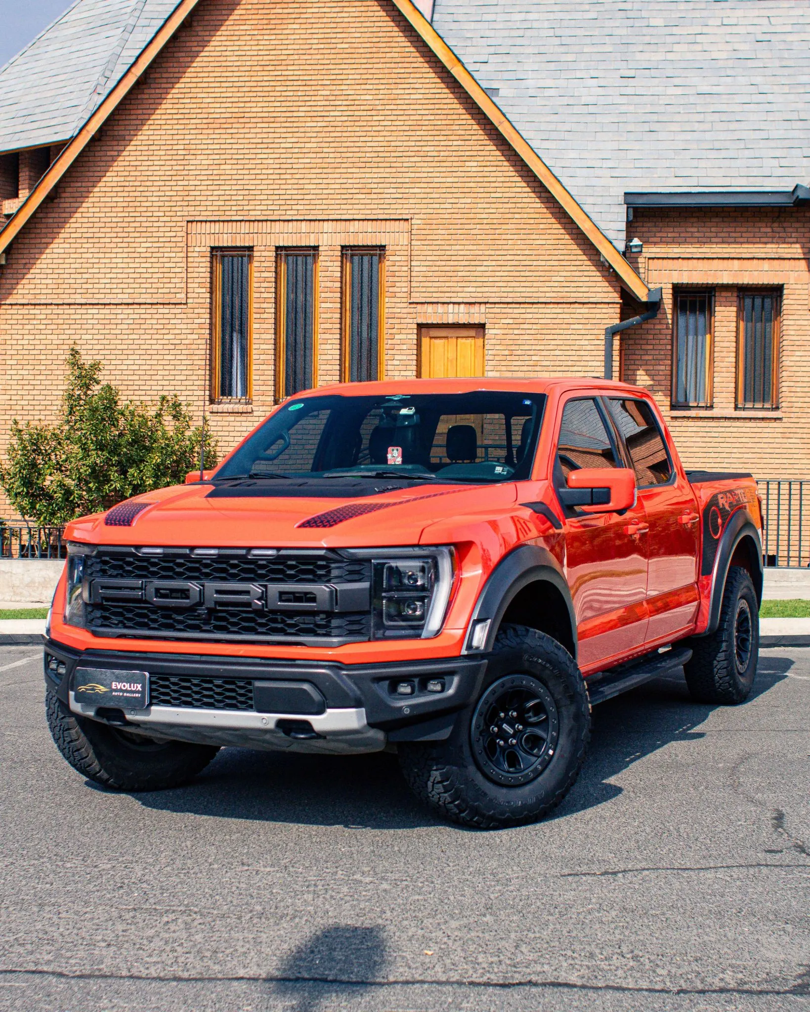 Detalle frontal de Ford F-150 Raptor naranja con parrilla negra, faros y placa Evolux
