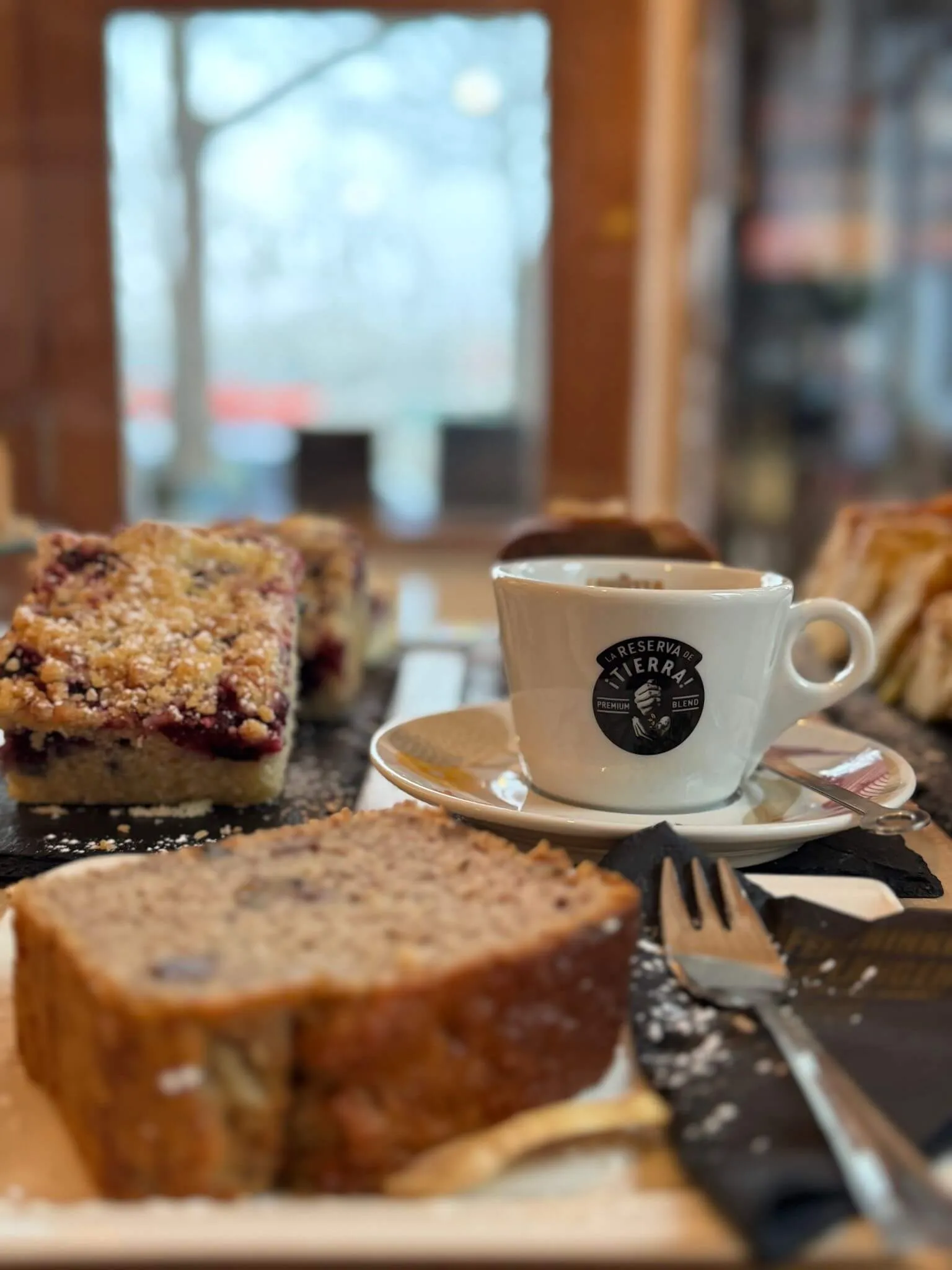 A cozy table setting featuring a cup of coffee, a slice of bread, and pastries, with a window view in the background.