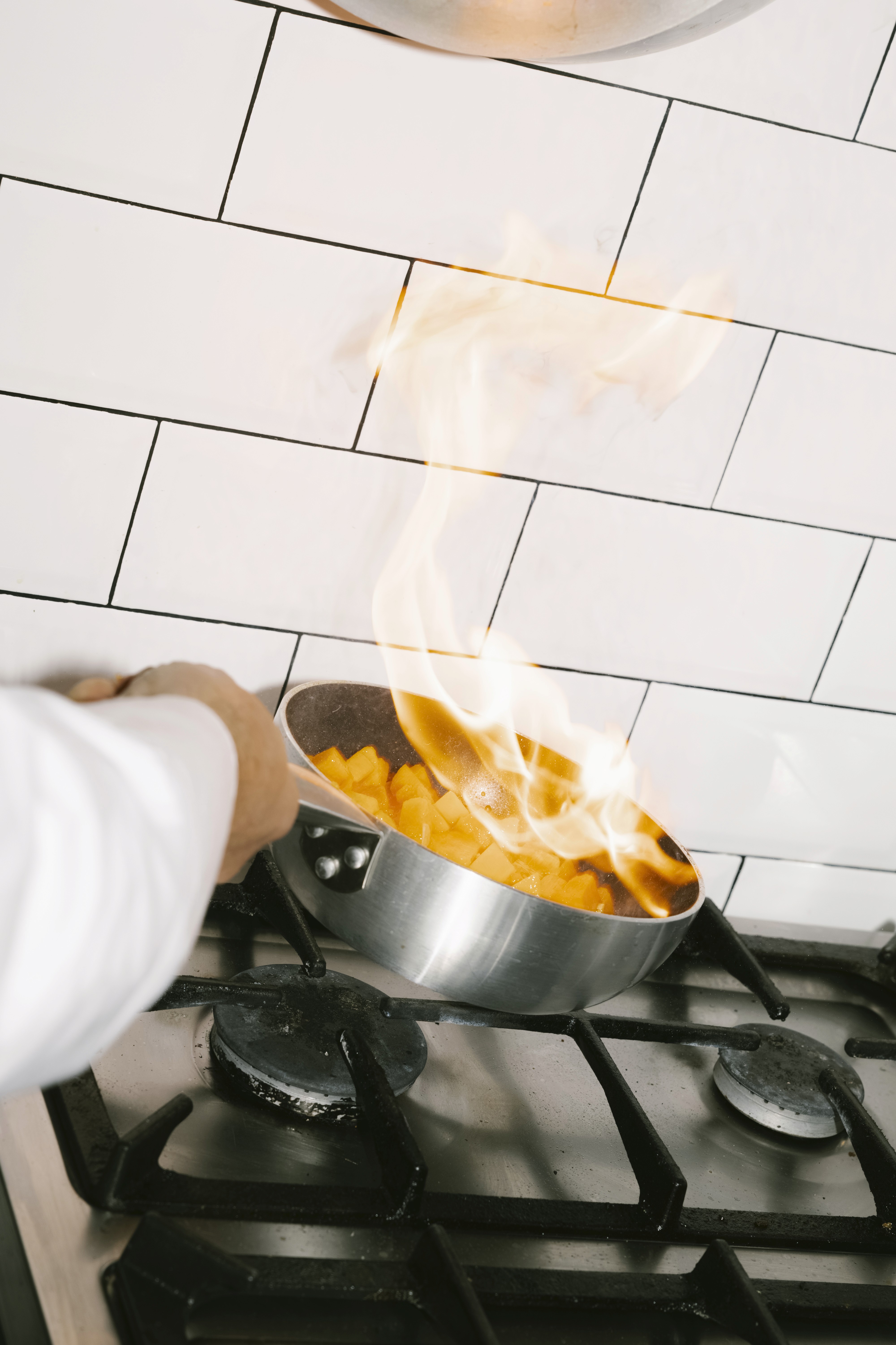 A chef flambéing food in a pan on a gas stove