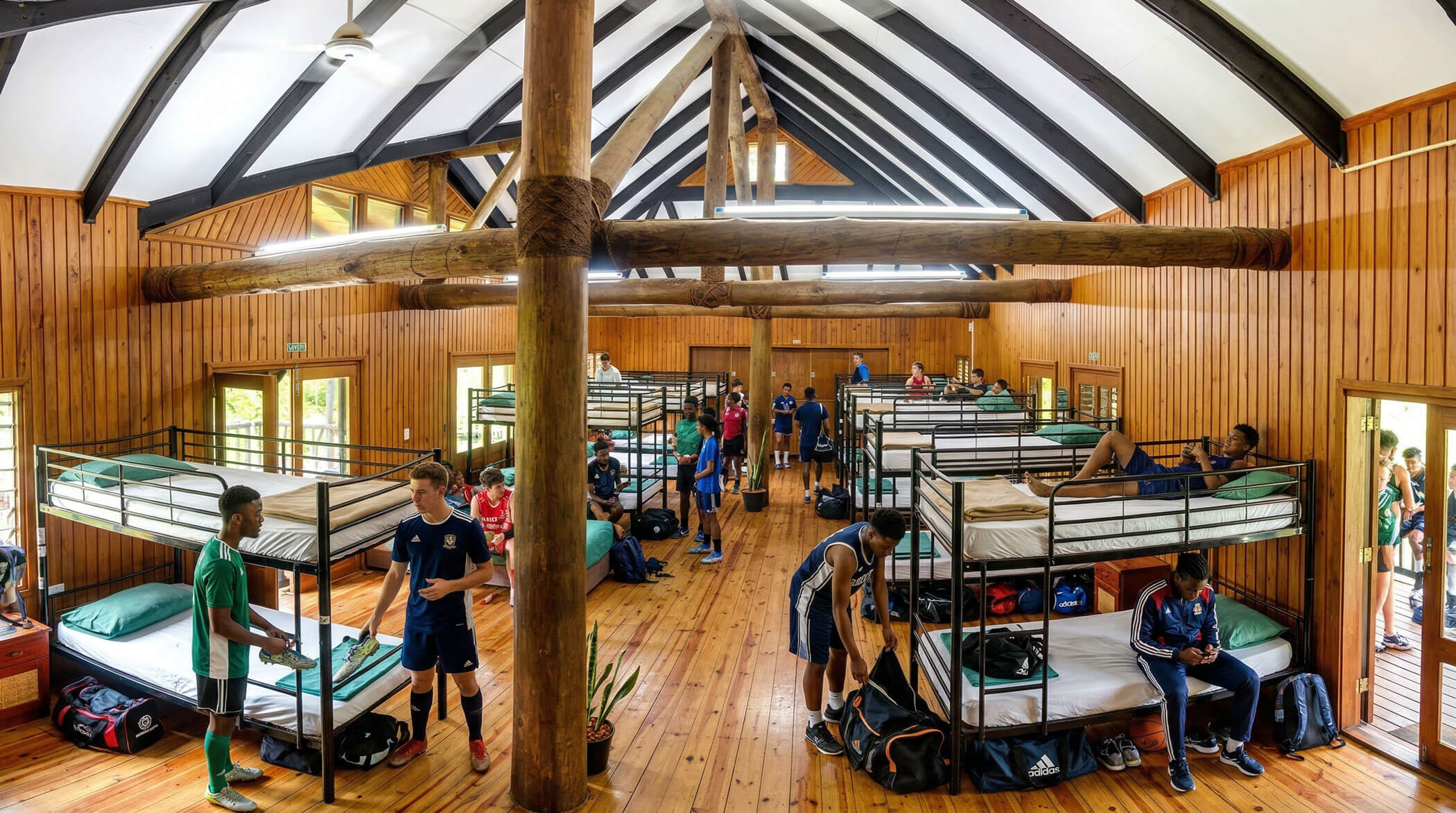 Spacious dormitory with multiple bunk beds, young men in sports attire resting and interacting at Uprising Resort, Fiji