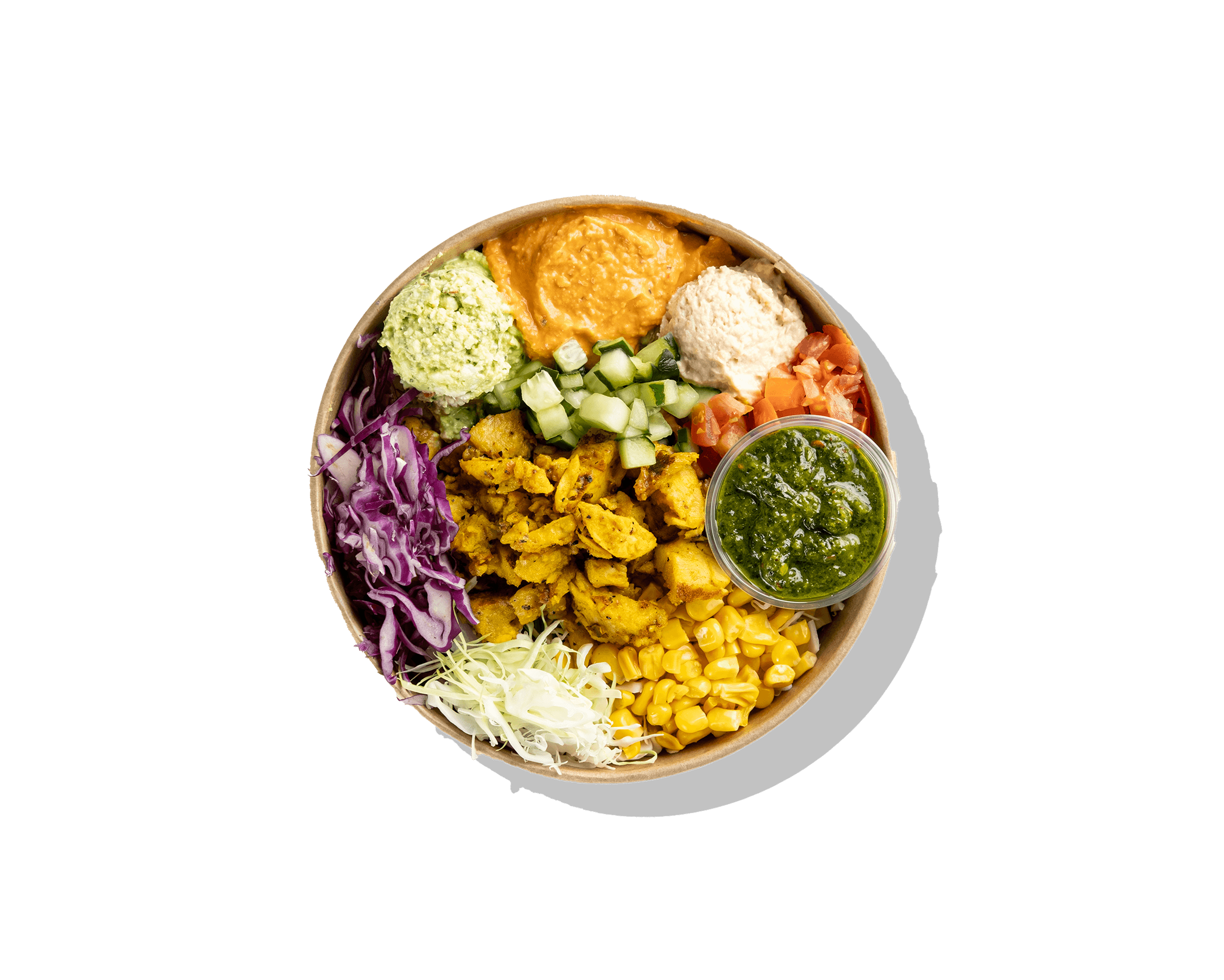 top down shot of a bowl with chicken shawarma, various vegtables, hummus, and a small container of sauce