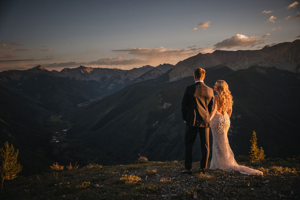 Newlyweds looking across a mountain valley at sunset