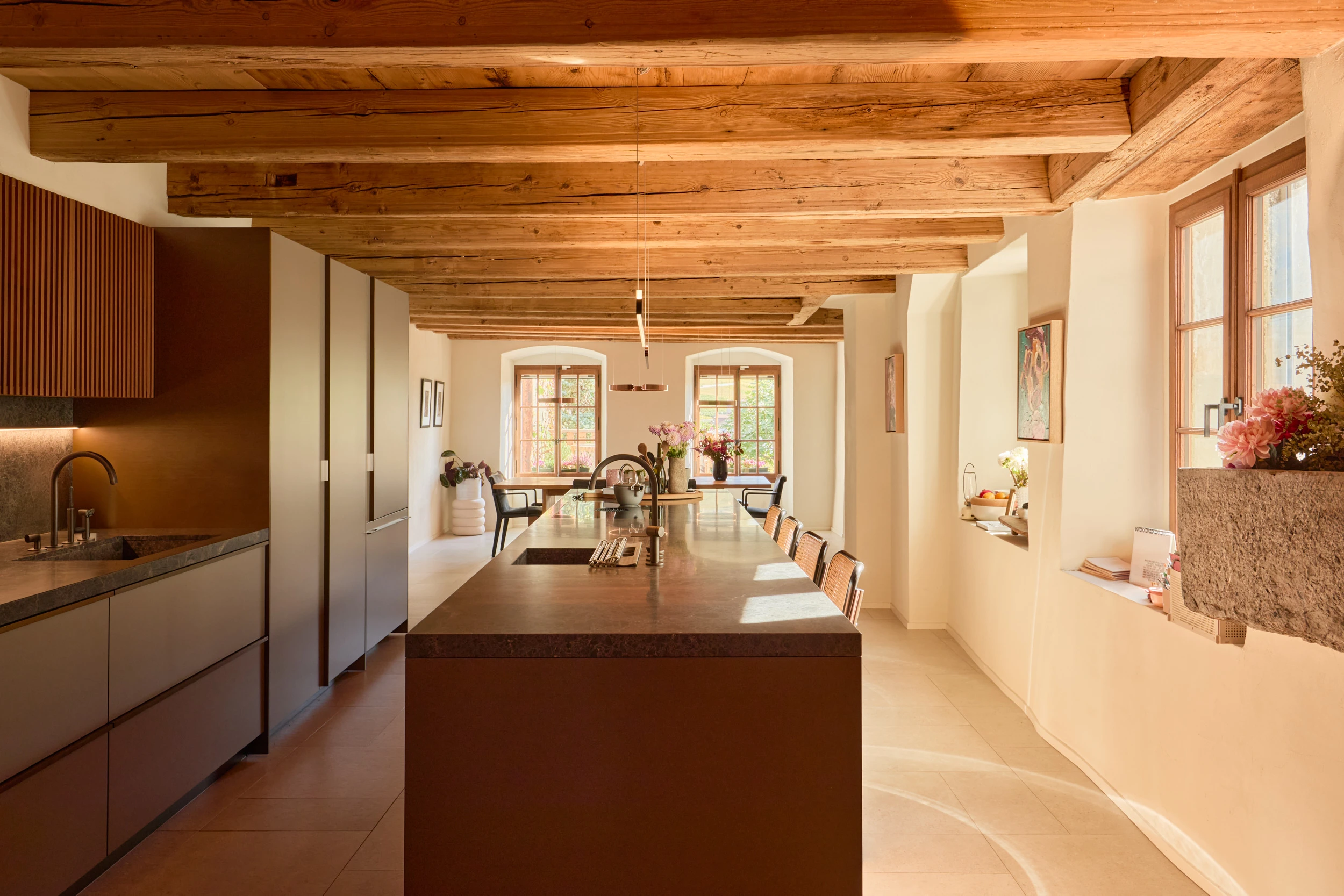 Cuisine Dada de Vincent Van Duysen dans la maison Muriset à Cully, intégrée à un intérieur historique avec poutres du XVIIIᵉ siècle, enduits à la chaux, sol en pierre et évier en pierre de Saint-Triphon conservé.