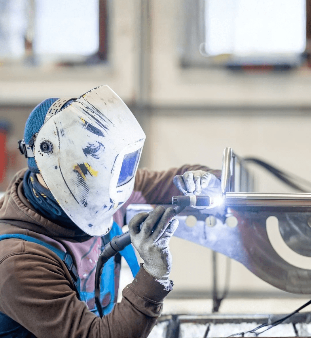 A man in personal protective equipment is welding custom stainless steel boat rack