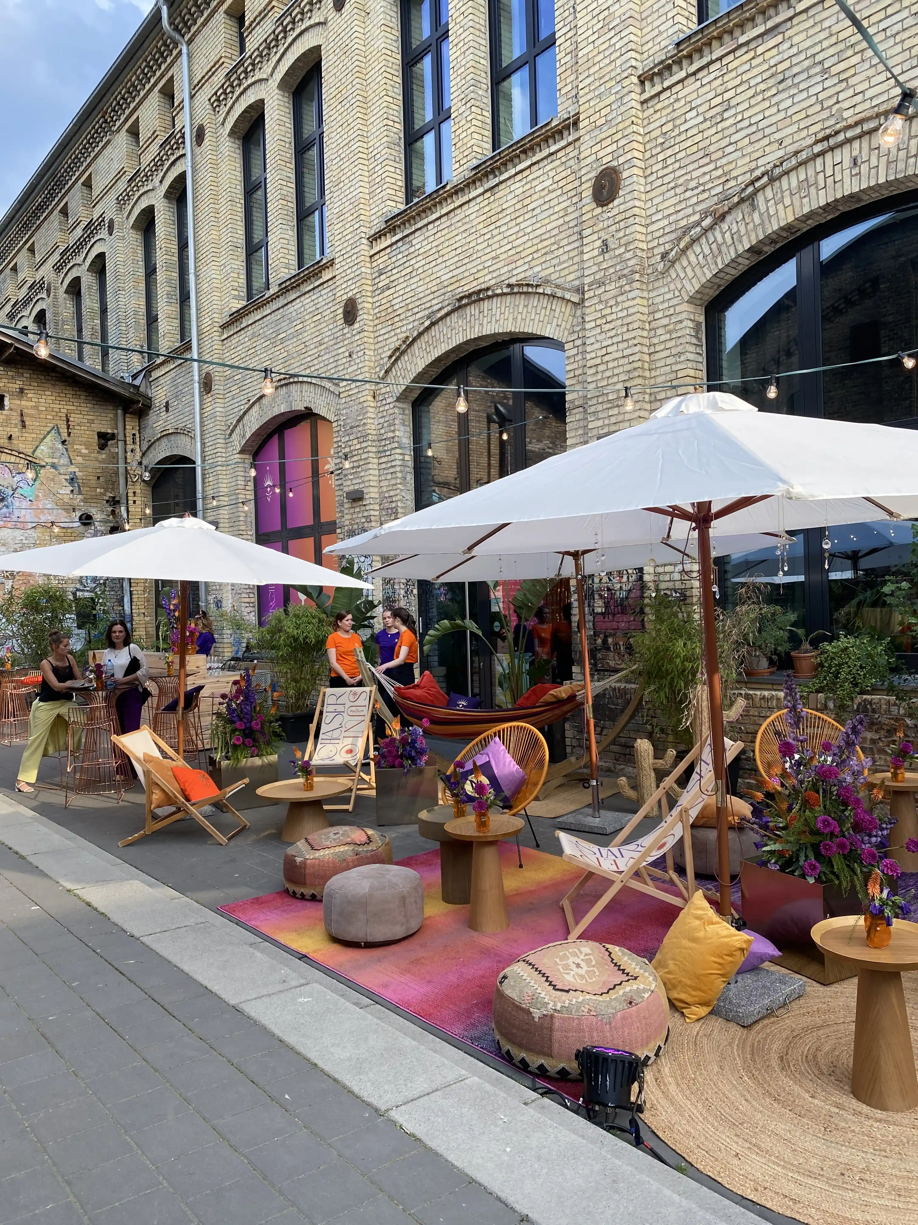 Colourful outdoor lounge with parasols, deck chairs, hammocks and rugs in a brick courtyard.