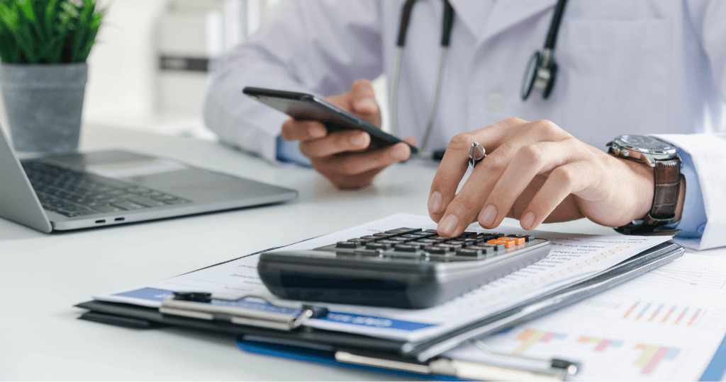 Doctor calculating clinic finances with charts and devices.