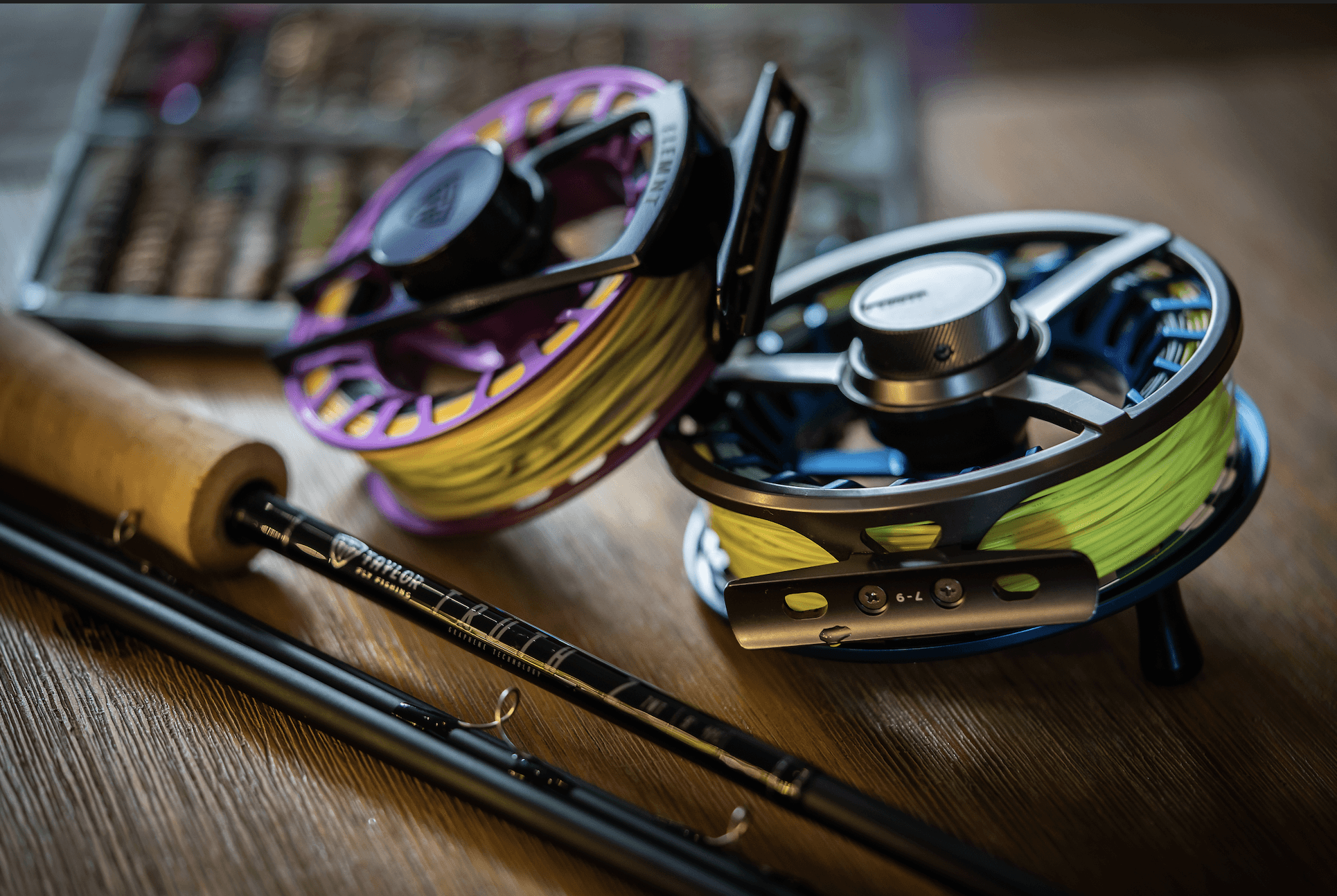 fly fishing rod and reel sitting on a table with open fly box. Pink fly fishing reel. blue fly fishing reel