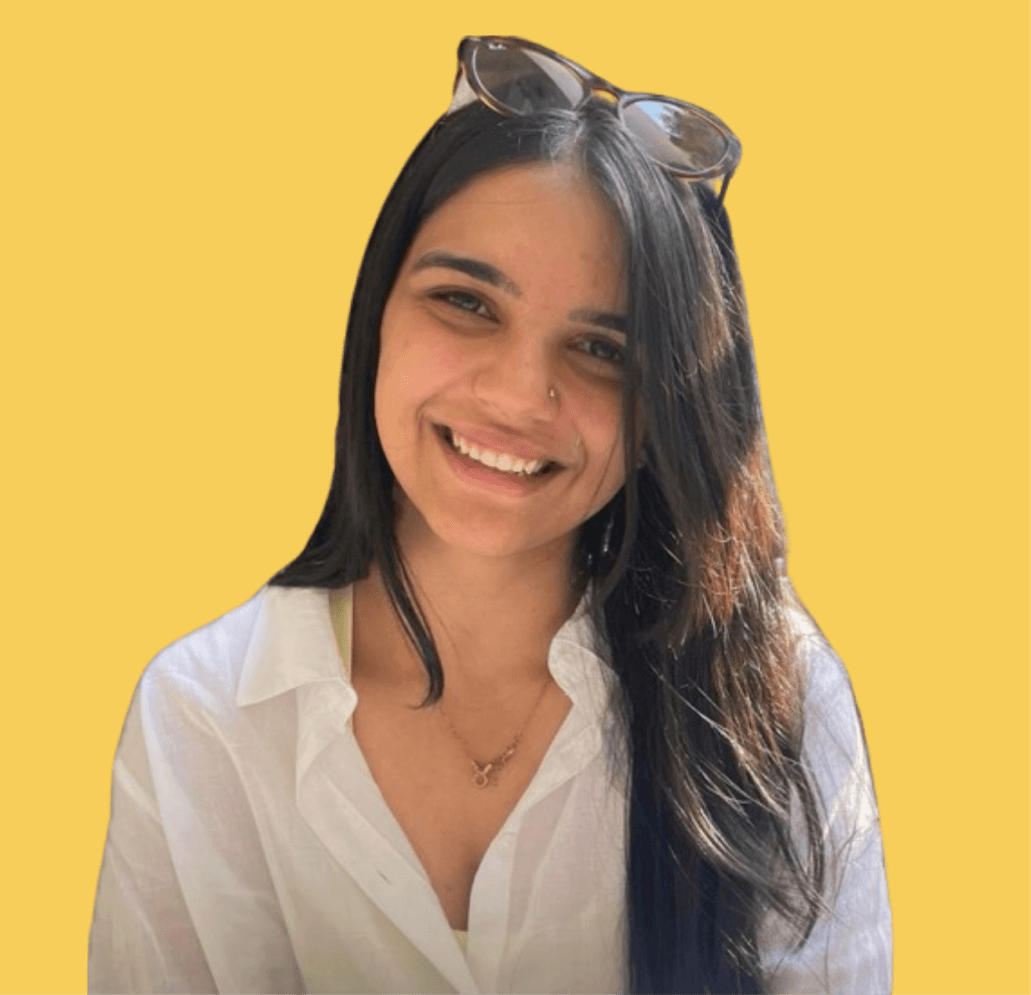 A smiling photo of me with long, dark hair is wearing a white shirt and sunglasses perched on her head. She has a warm expression and is looking directly at the camera. The background is a solid yellow color.