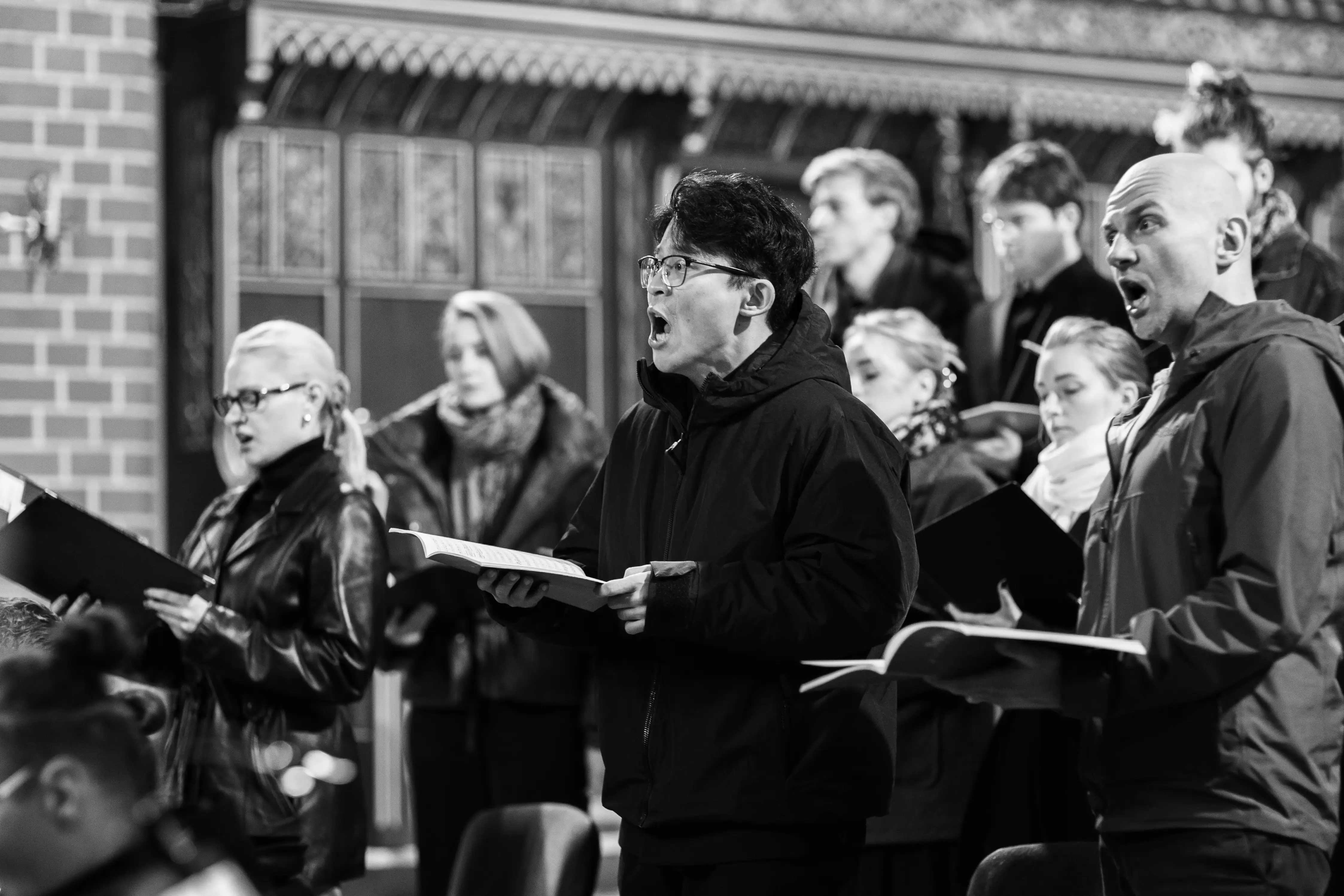 Śpiewający chór w kościele. W centum znajduje się mężczyzna z otwartym śpiewnikiem w ręku.