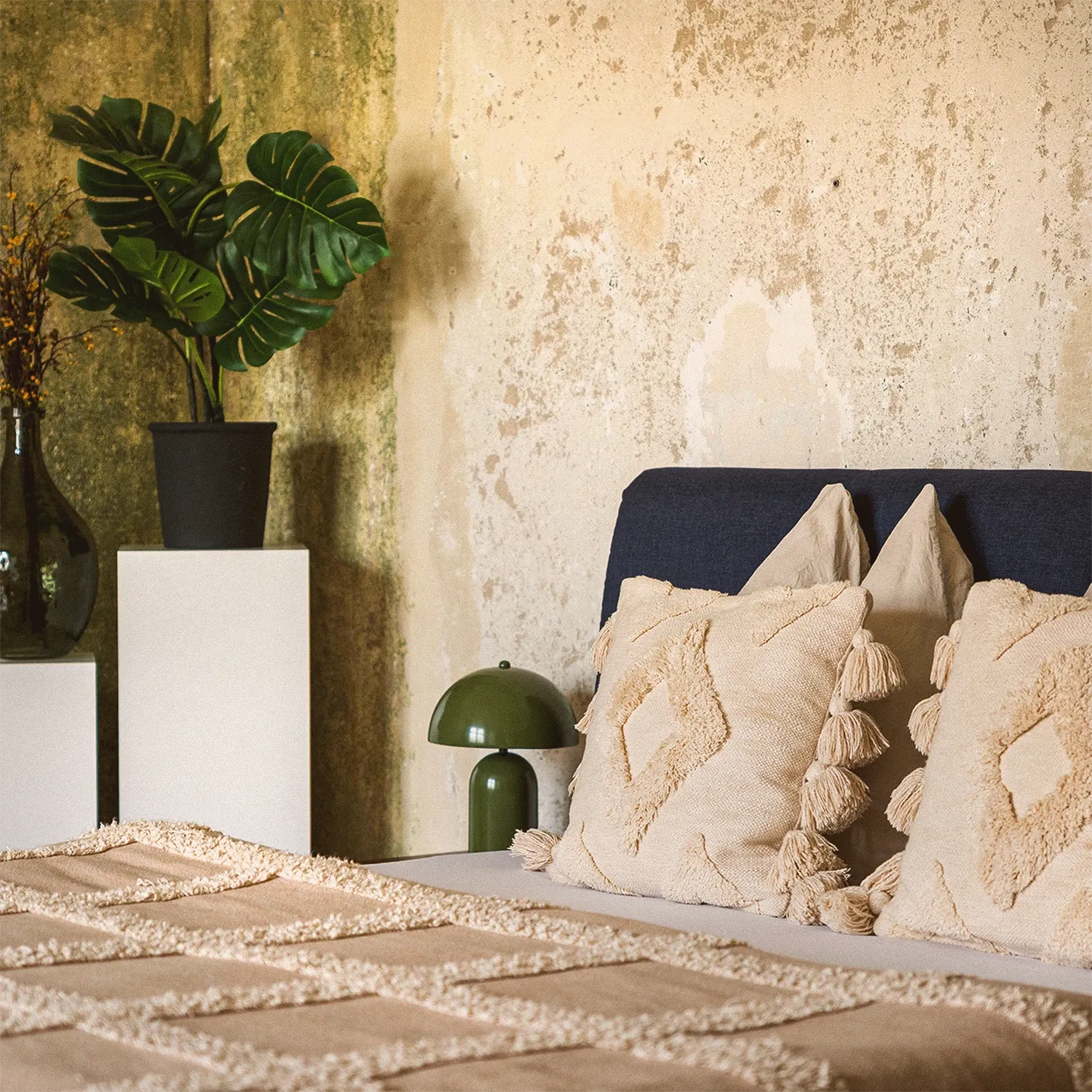 Boutique N°1 • bed with a navy headboard, tufted cushions and a green table lamp in front of a weathered wall