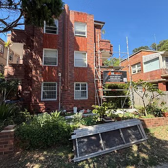 Scaffolding erected on the side of a multi-storey brick residential building during remedial construction works, with a Hitech Remedial Group signboard visible