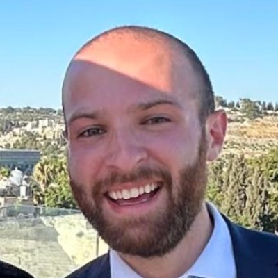 A smiling person with short, dark hair and a light-colored shirt against a dark background.