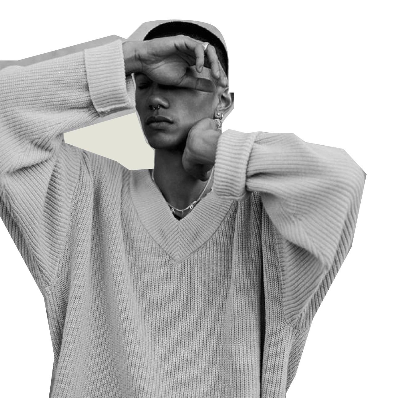 Black and white portrait of a person in an oversized knit sweater, raising one hand to partially cover their eyes.