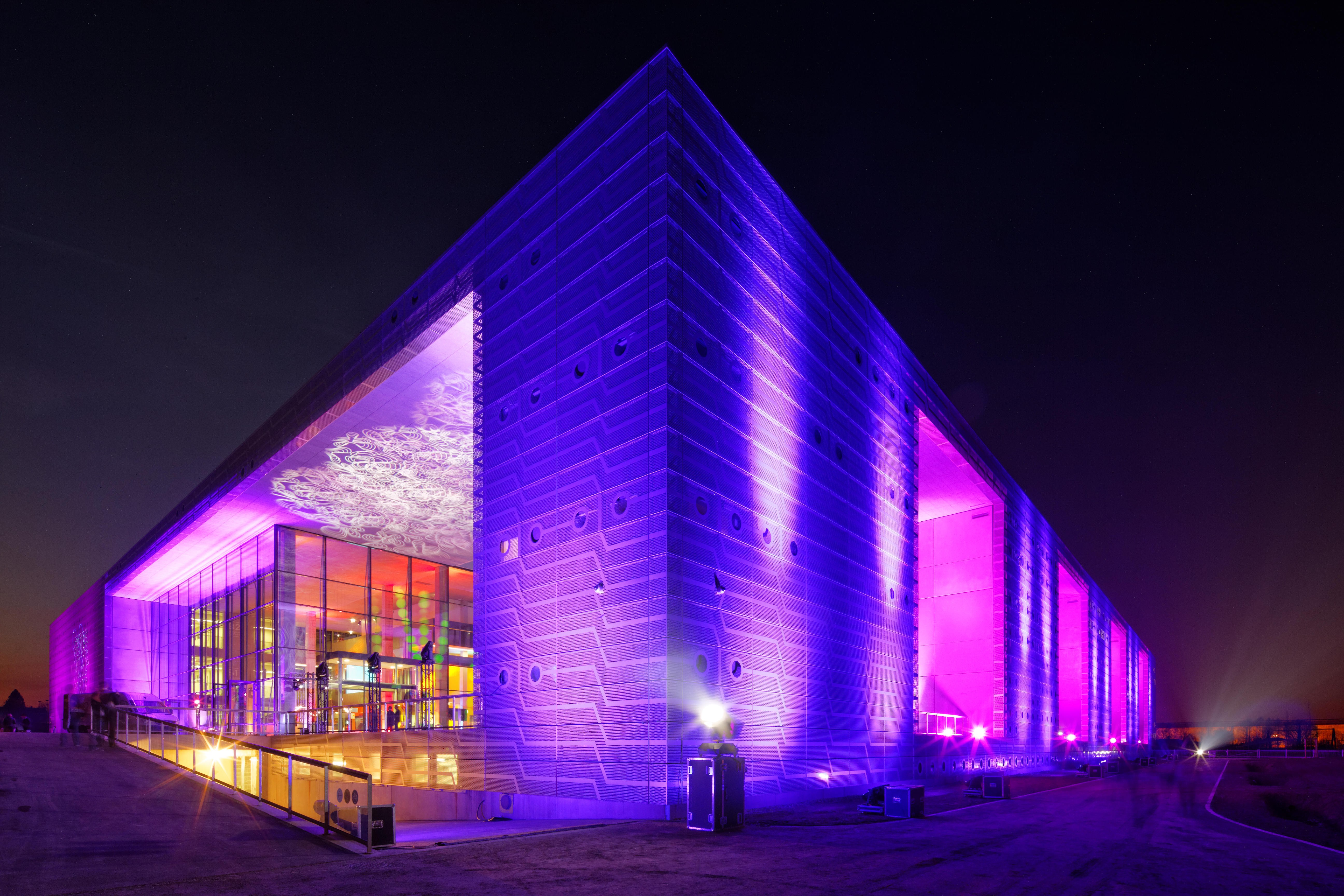 Bâtiment moderne illuminé de violet et rose la nuit. Architecture contemporaine.