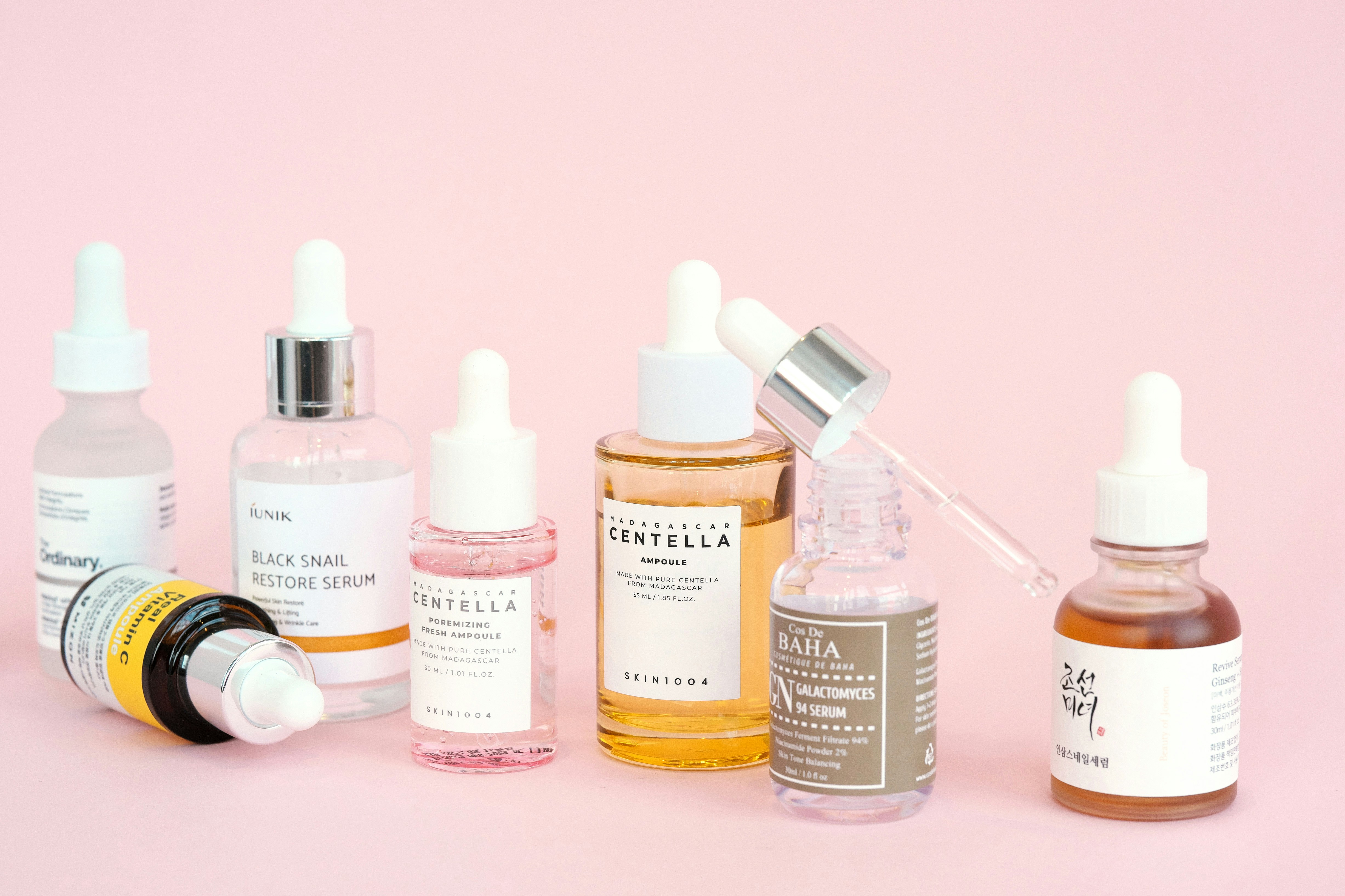 Skincare products, including serums, arranged on pink.