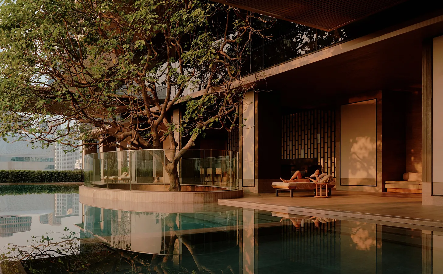 A sunset photo of a guest resting on a patio chair at Aman Nai Lert Bangkok's rooftop pool