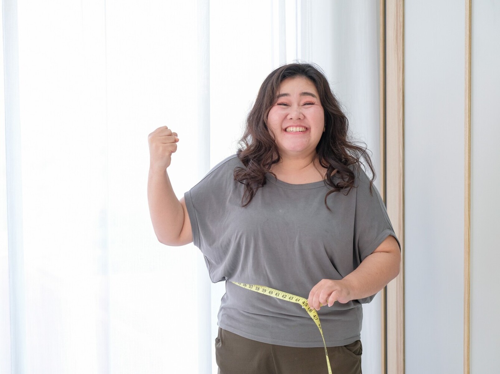 overweight woman smiling as she measures her waist after losing weight with pilates