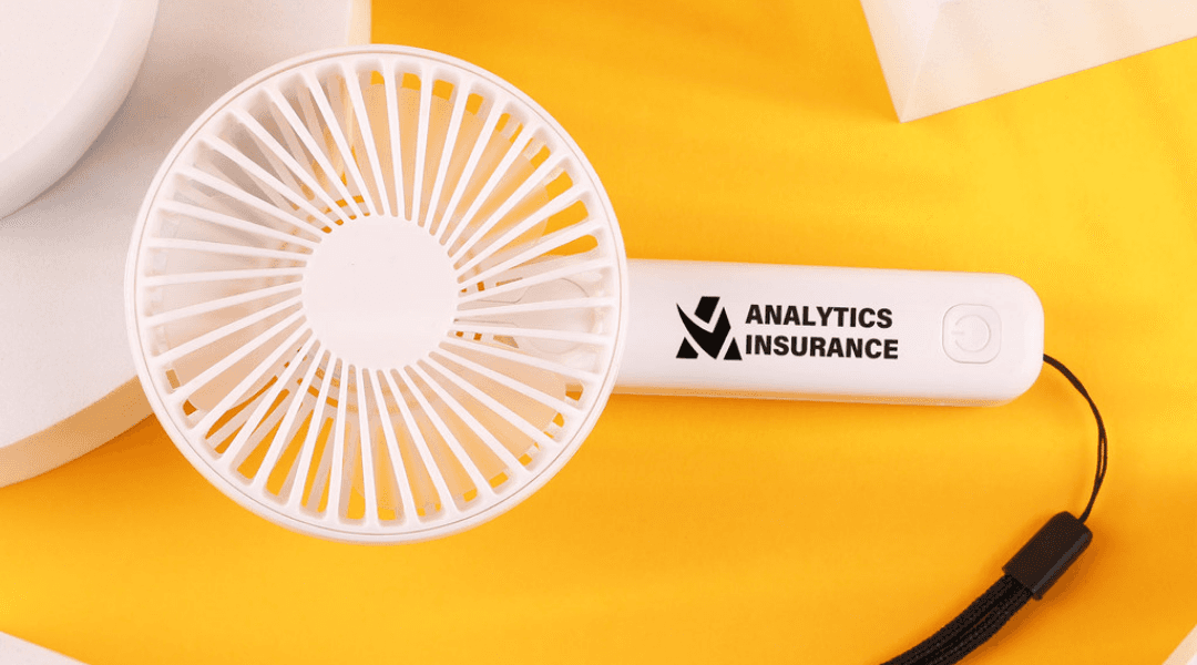 A white mini mechanical fan with a log on the handle sitting on a yellow table
