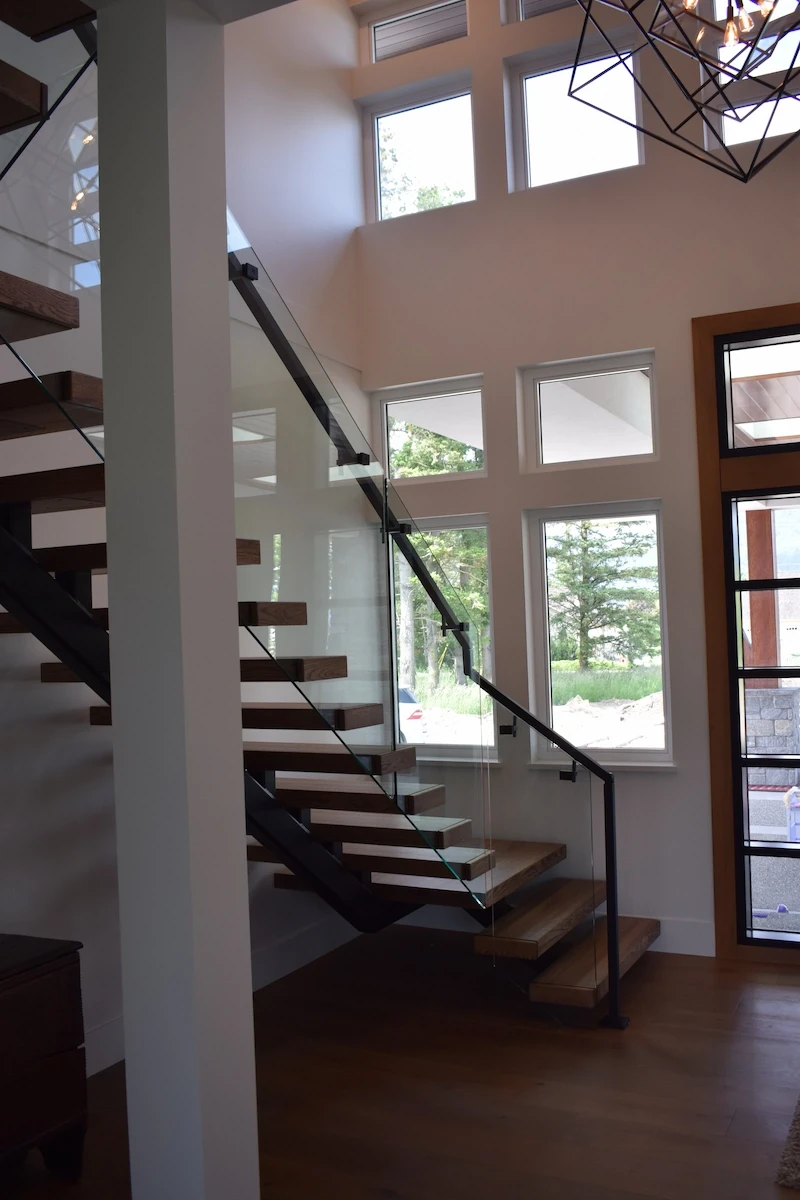 A modern floating staircase with frameless glass railings and black handrails.