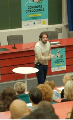 Un orateur s’exprime au pupitre devant une salle réunie.