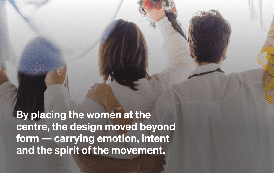 Black-and-white photo of women embracing from behind, one raising a colourful headscarf, overlaid with a quote about placing women at the centre of the design.