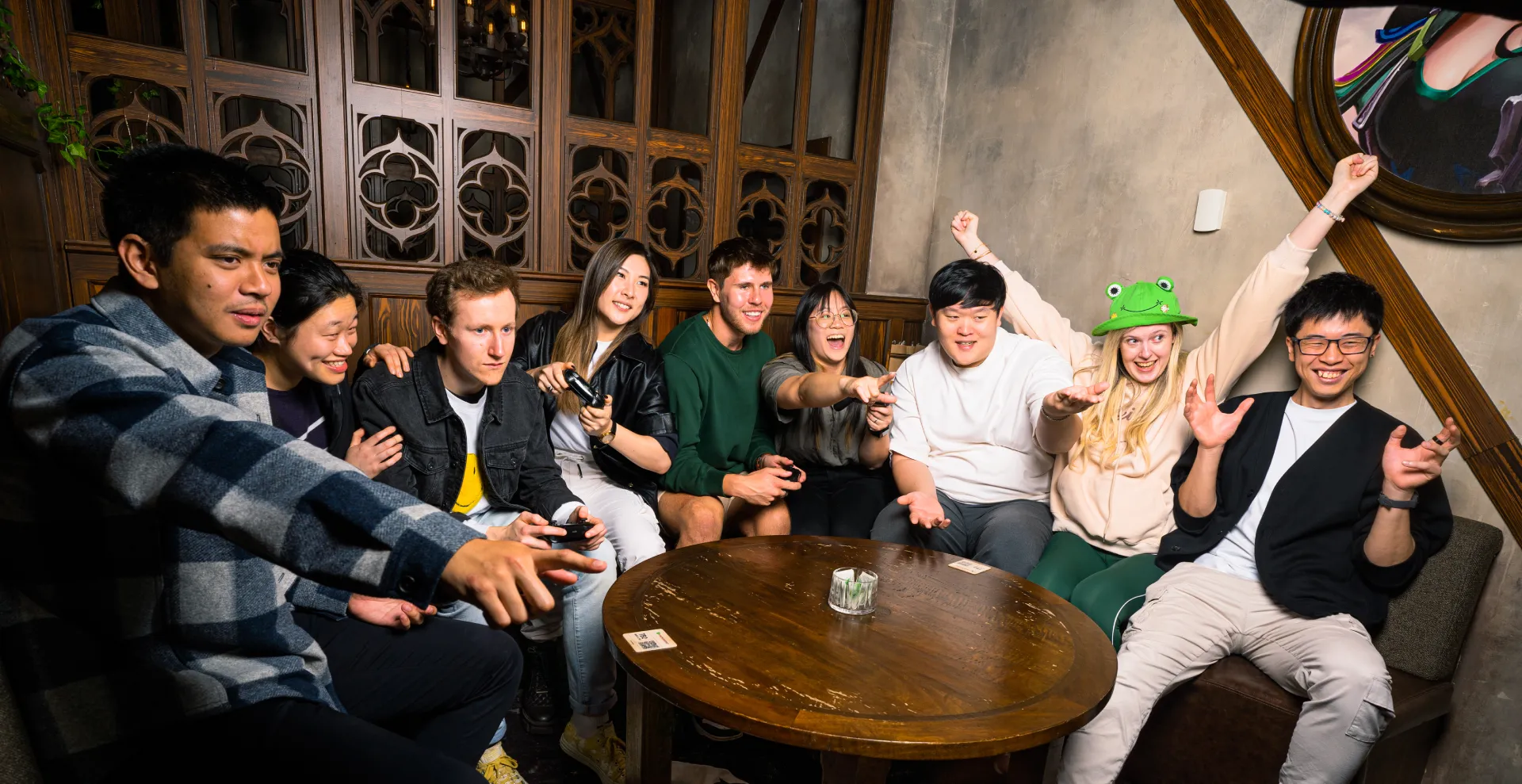 A group of people with their attention off screen, with some of them holding video game controllers in their hands, sitting around a round table