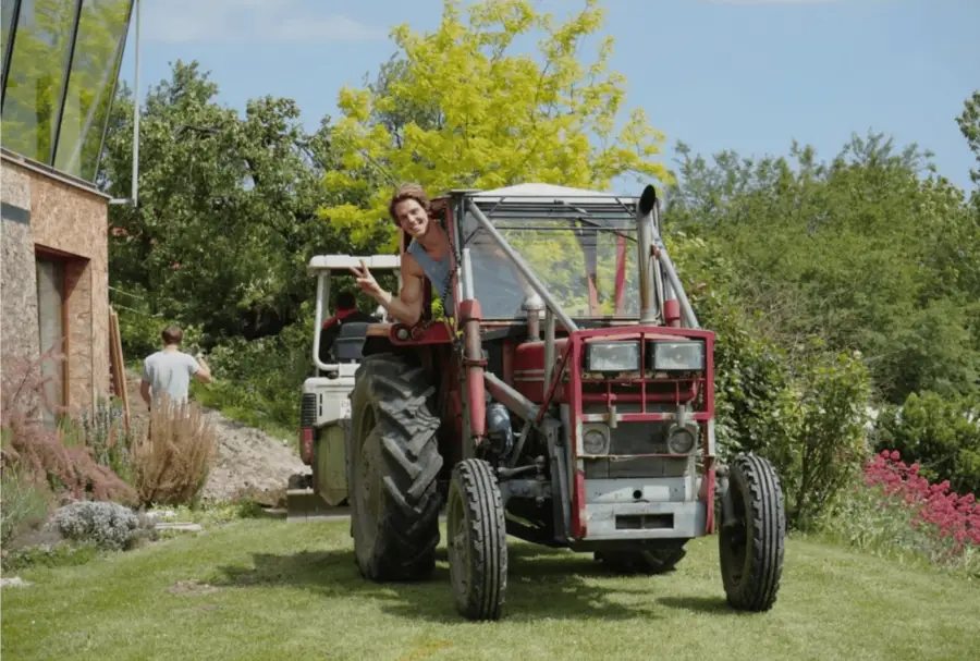 Markus Schmoltner winkt vom alten roten Traktor im Garten neben dem Chalet.