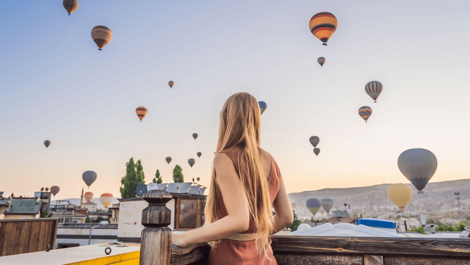 Hot air balloons over Cappadocia, Türkiye at sunrise viewed by a traveler