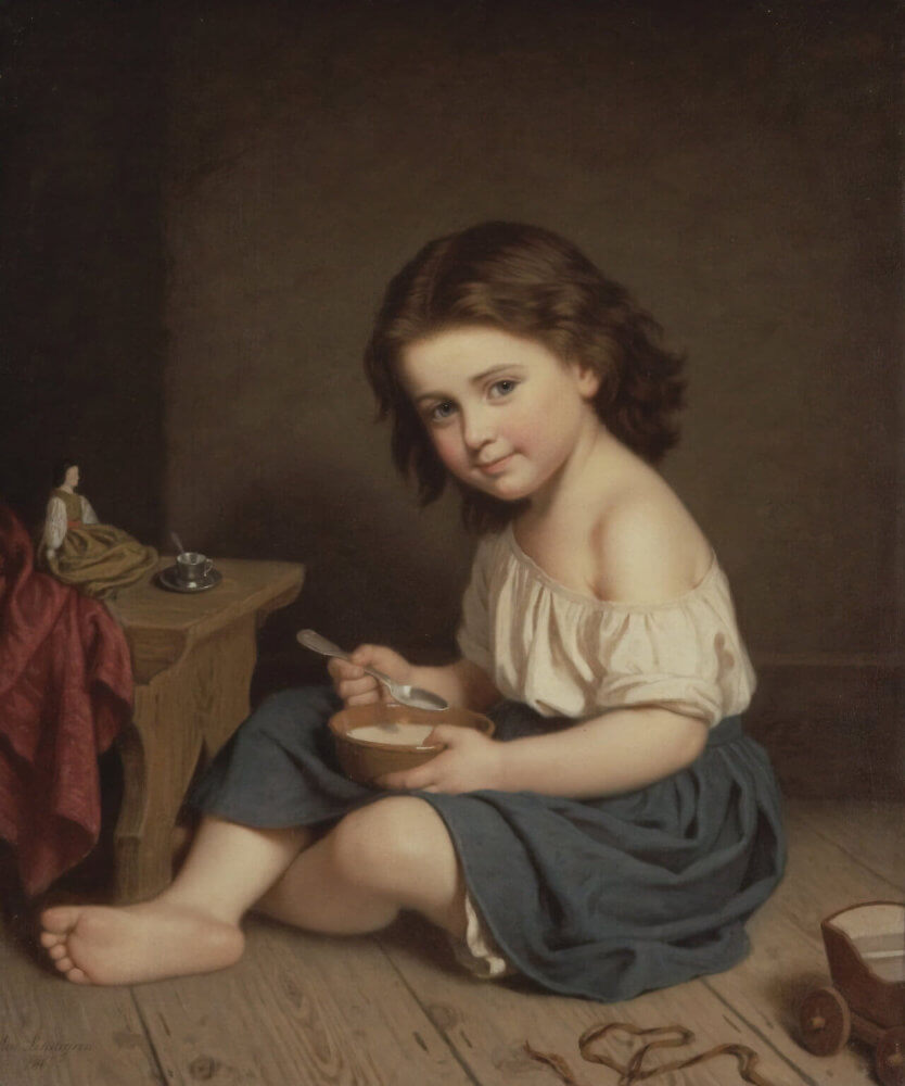 A young child sits on the floor, holding a bowl, with a simple backdrop and a few scattered items nearby.