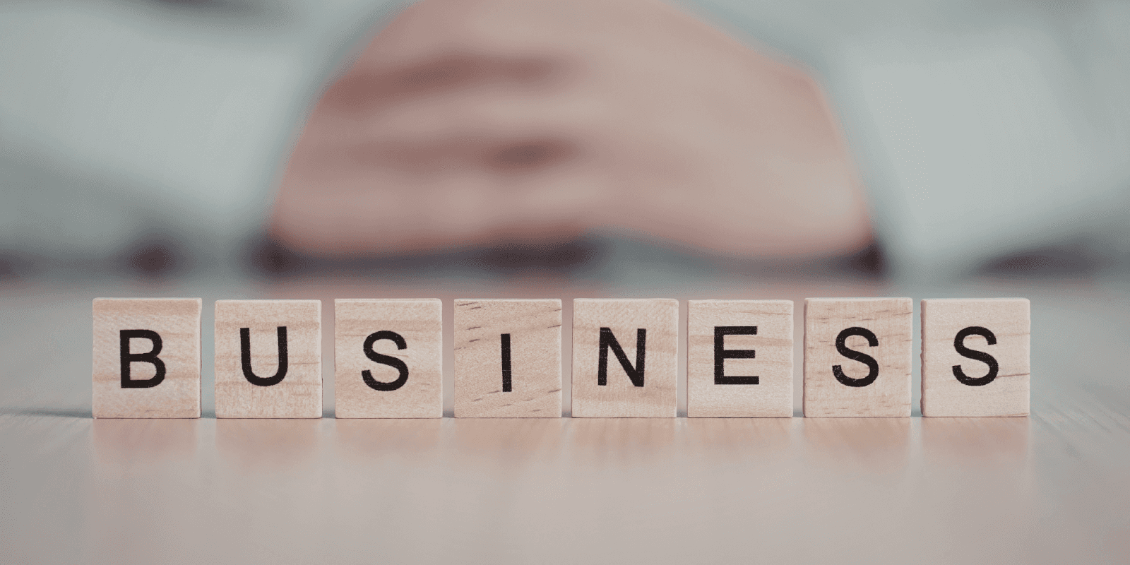 Wooden blocks spelling “BUSINESS” on table with blurred person in background, symbolizing strategy and growth.