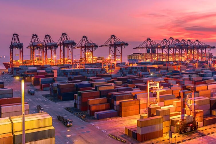 Shipping port with cranes and stacked cargo containers at sunset