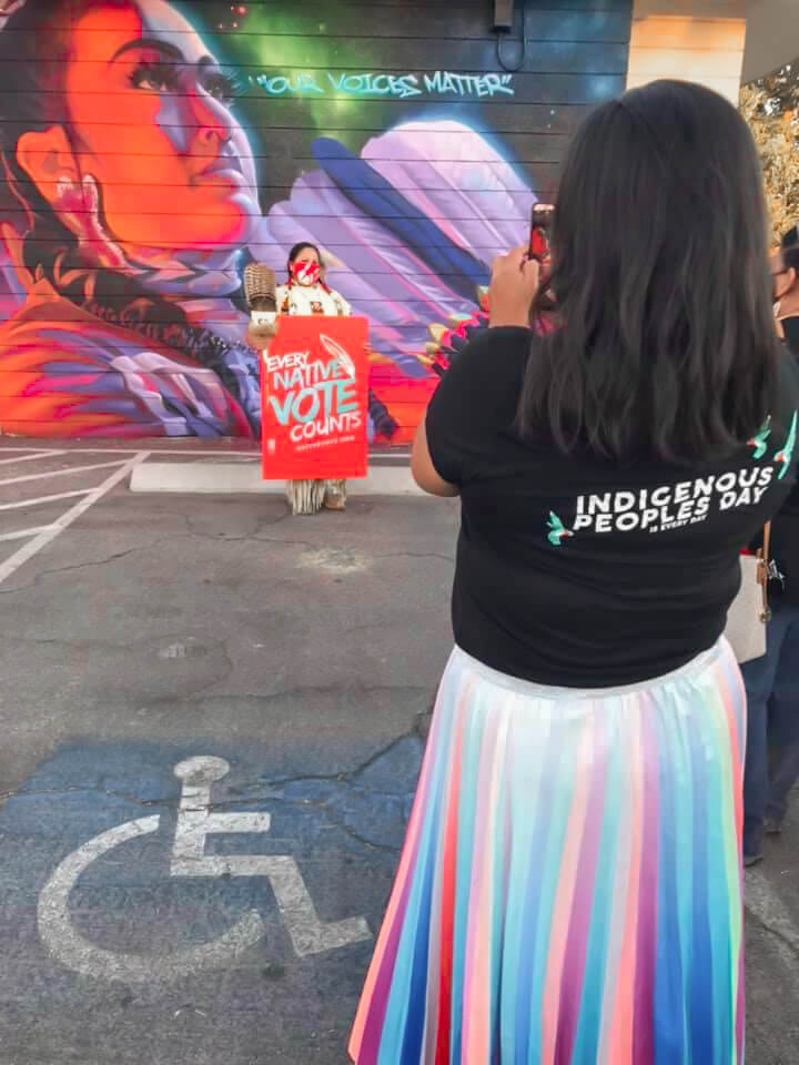 Girl taking photo of another woman holding sign of Every Native Vote counts
