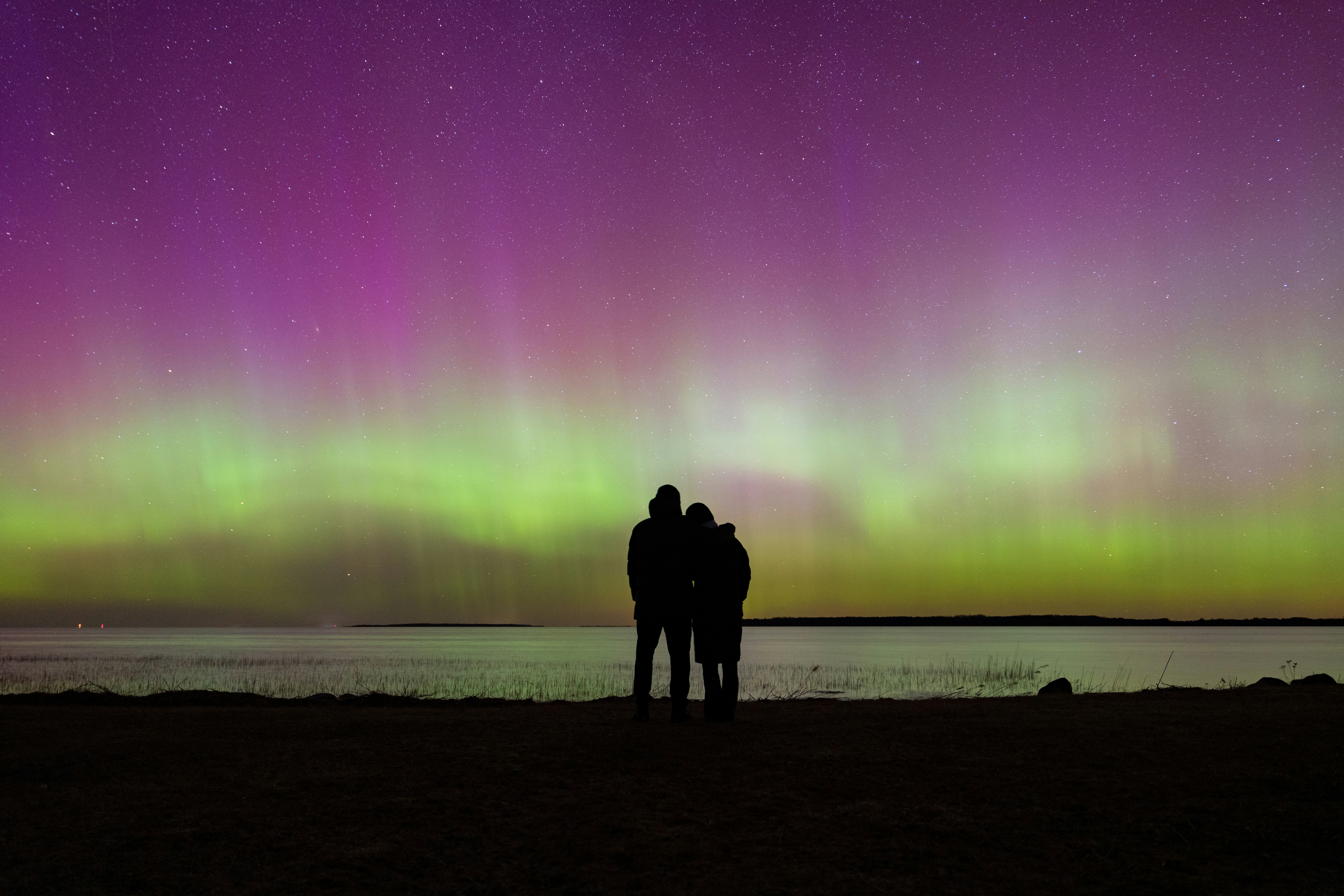 A couple watching the Northern Lights over a river.
