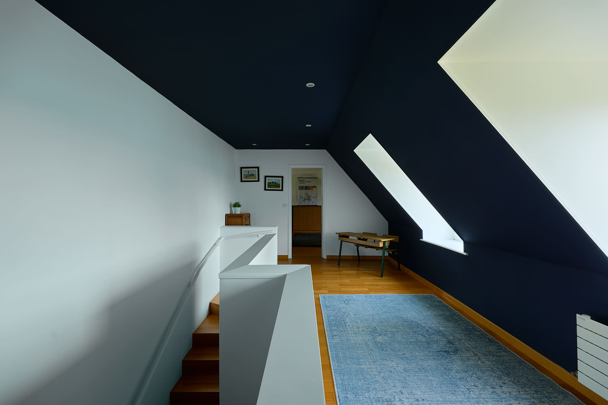 Palier bleu l'arriver de l'escalier en bois solide par la gauche, avec un grand tapis bleu, mansarde peinte en bleu.