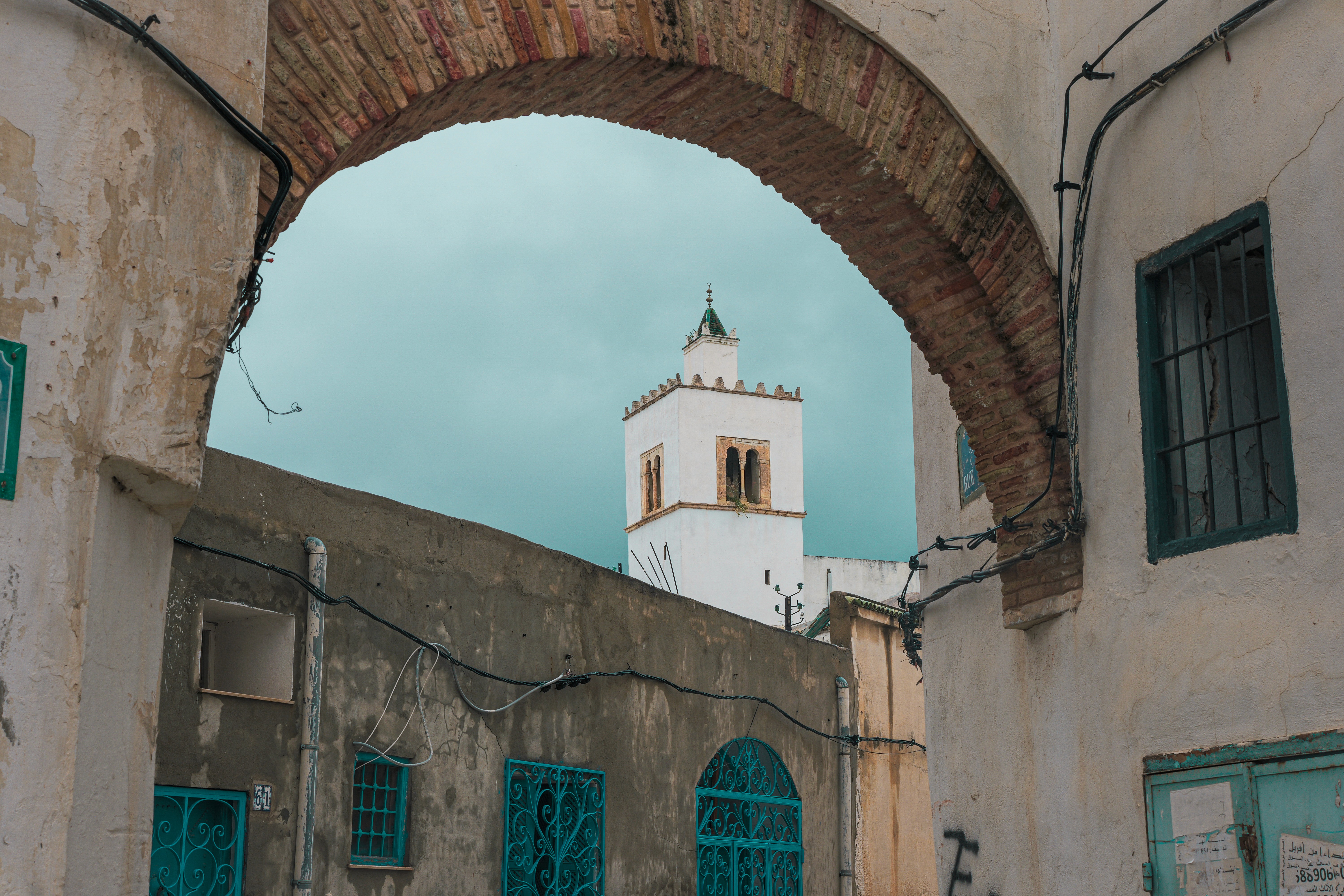 A small white motorboat cruises on turquoise water, leaving a wake, next to a massive, craggy white rock cliff formation under a hazy sky.
