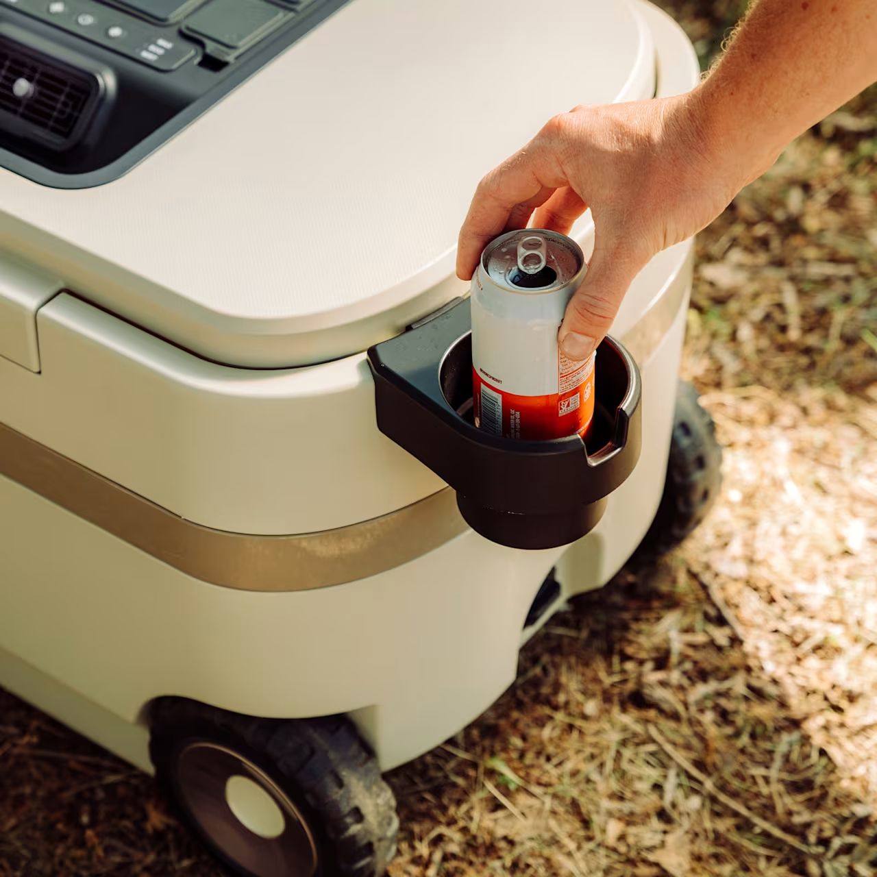 Hand placing a can into a black cup holder clipped to the side of a cream cooler