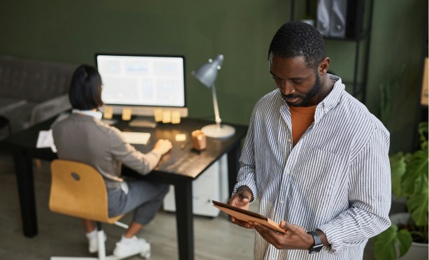 Two people in an office looking at a computer screen and a tablet