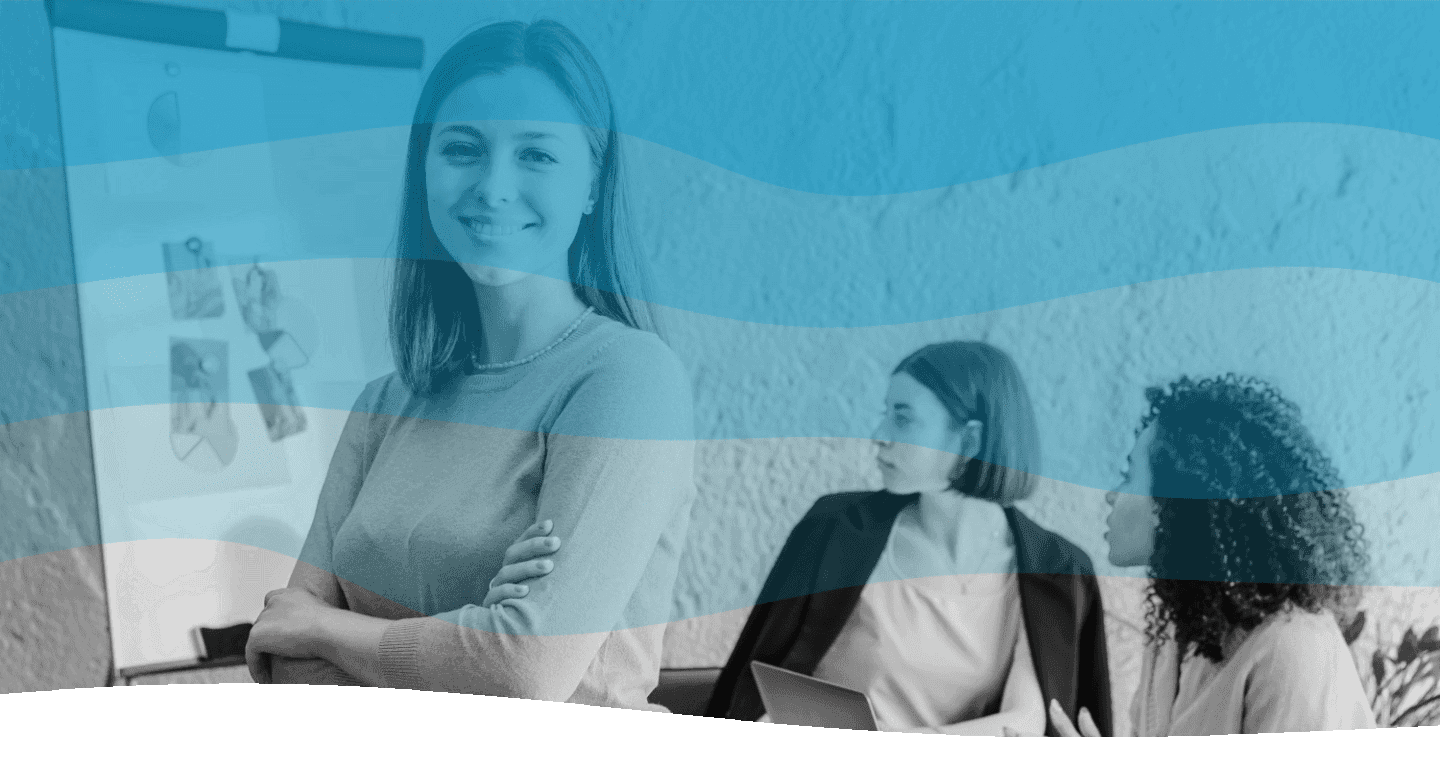 A group of diverse women in a professional meeting setting, with one woman standing confidently in front of a presentation board while two others sit and engage attentively, showcasing teamwork and collaboration.