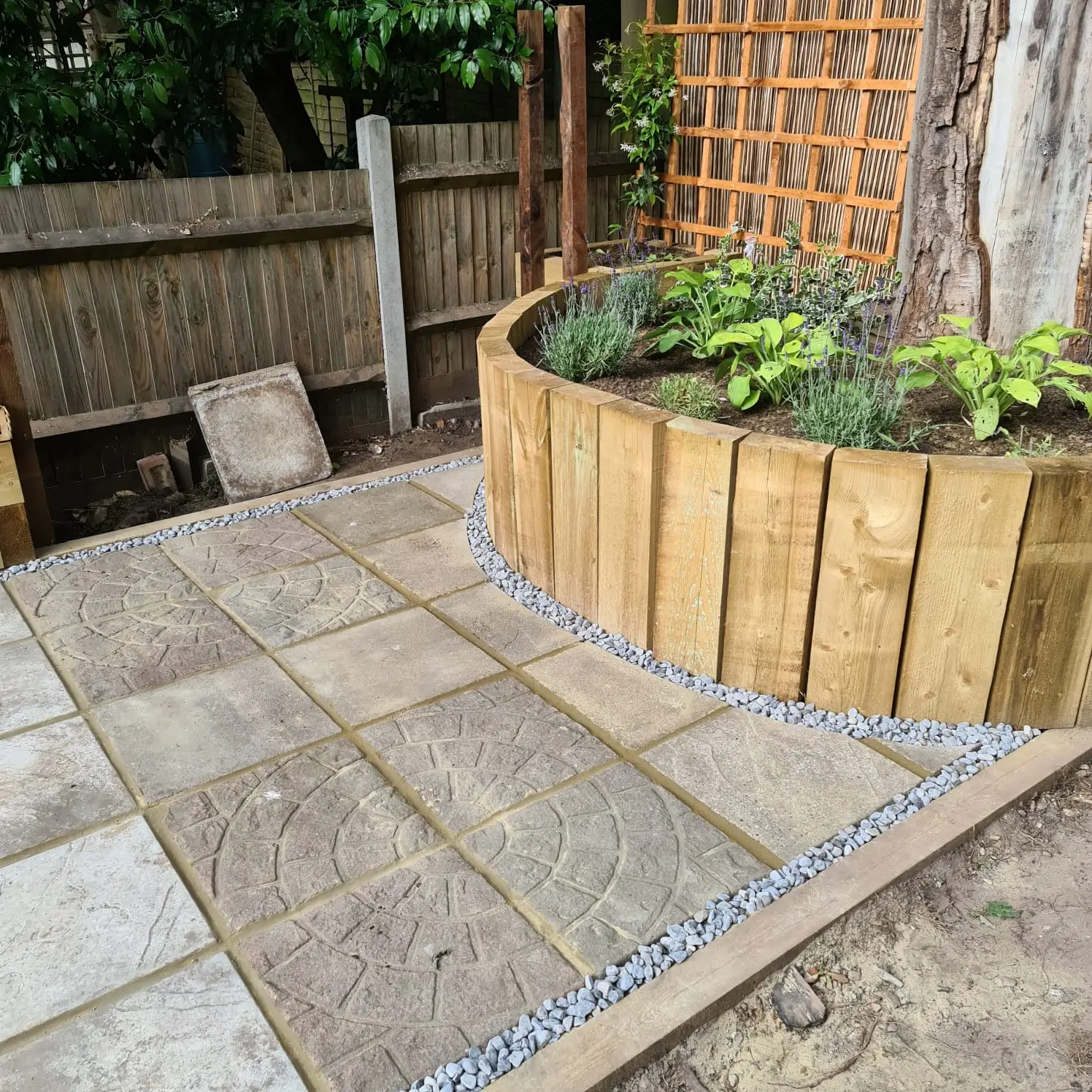 Garden area featuring stone paving, a wooden planter, and vibrant greenery in a tranquil outdoor setting.
